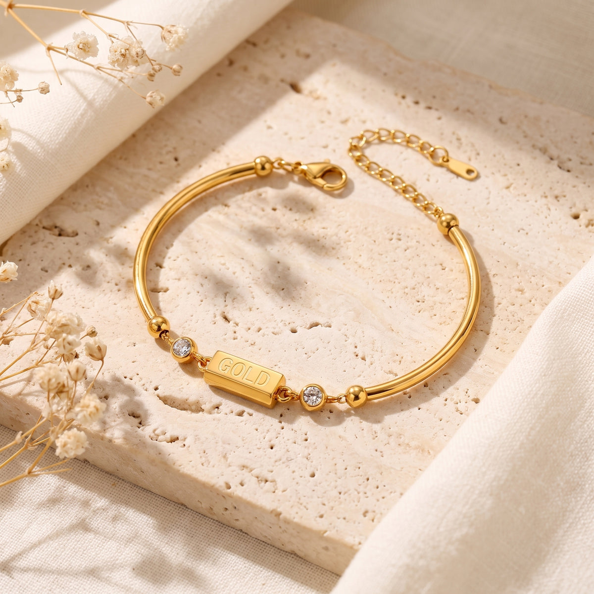 Gold-tone bar station bracelet with two round cubic zirconia accents on a beige stone surface.