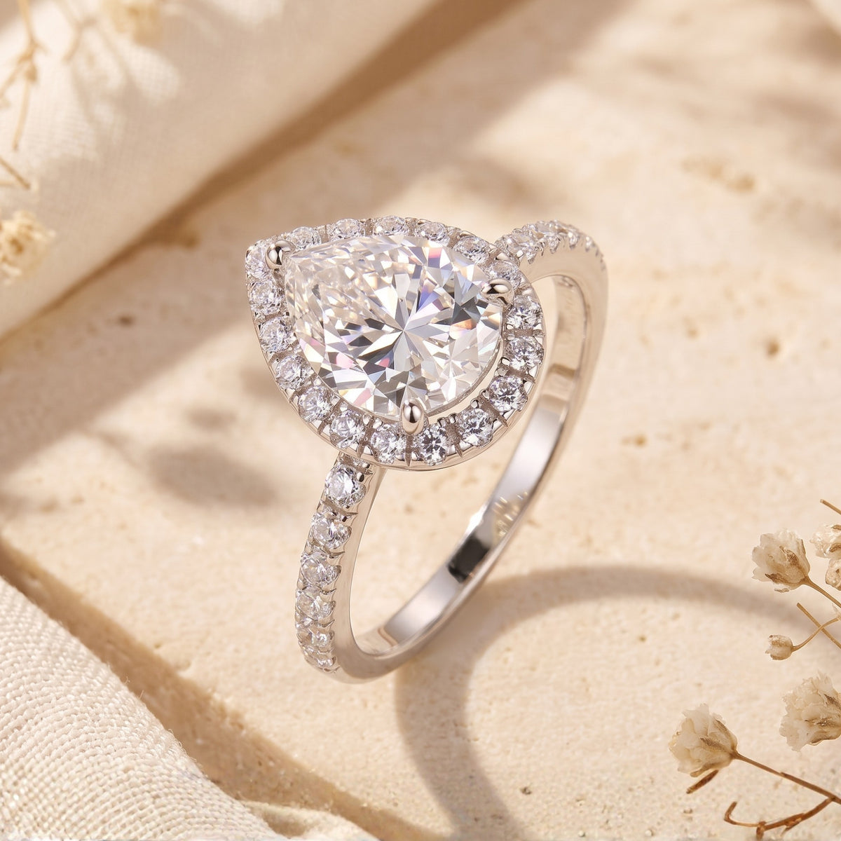 Close-up view of a silver ring with a pear-cut clear stone, pavé halo, and stone-accented band.