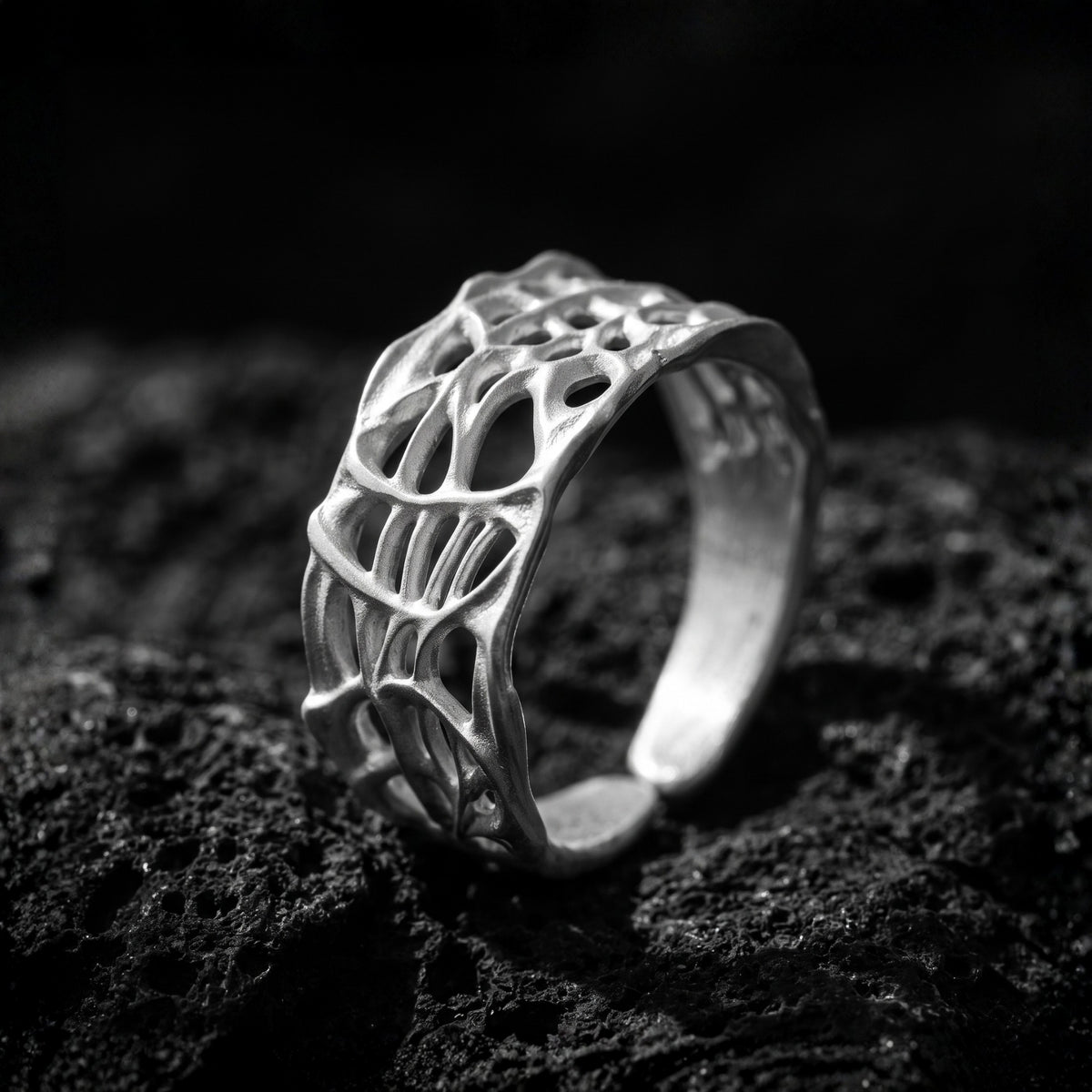 Angled close-up of the fine-silver open band ring with organic openwork, resting on rough dark rock.
