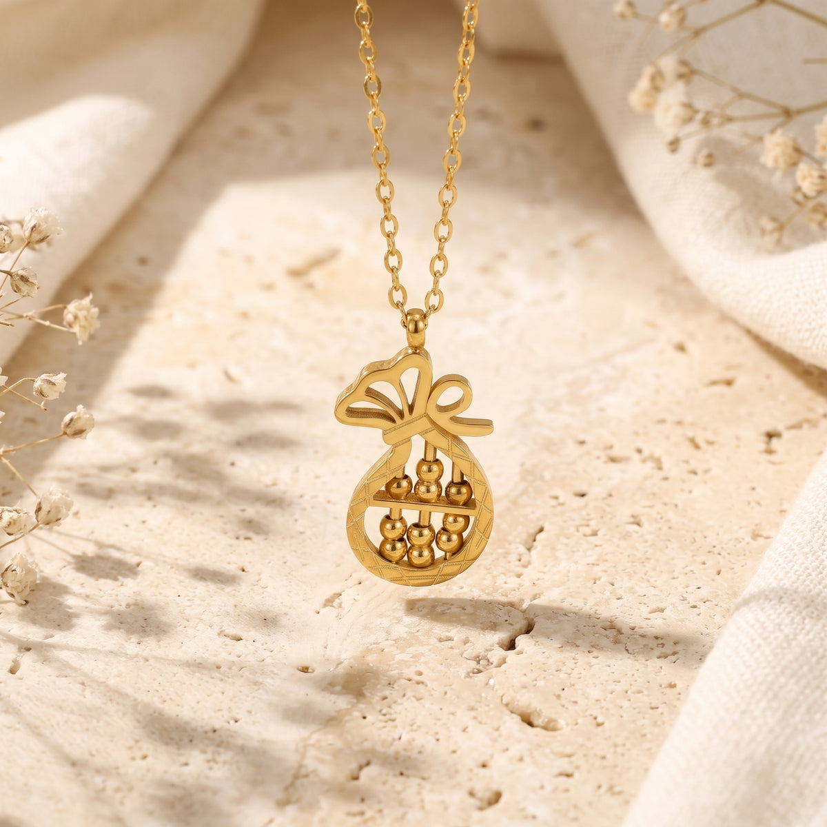 Macro view of gold-tone fortune bag abacus pendant hanging on a delicate chain.