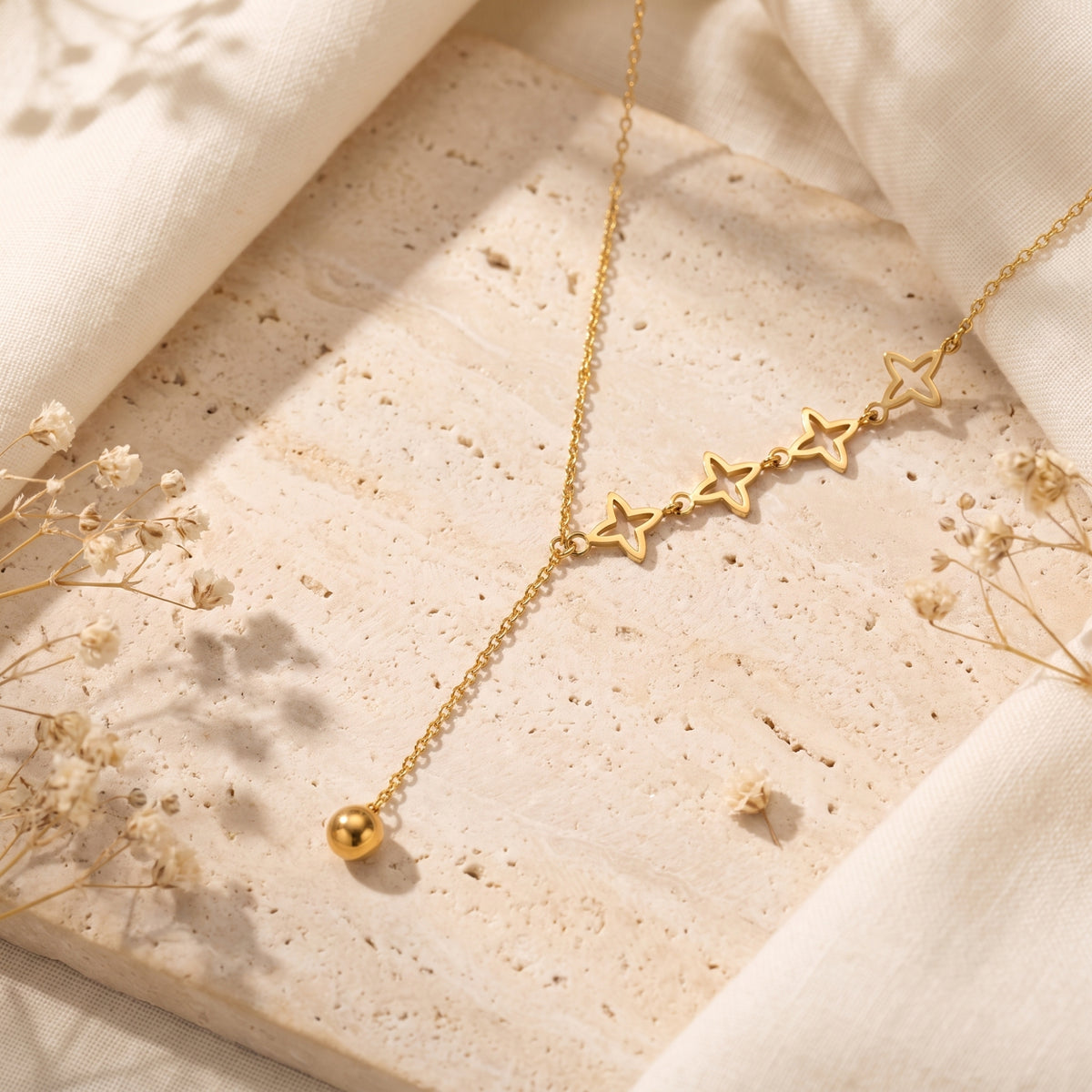 Gold-tone lariat necklace flat lay on a stone slab, showcasing four openwork star stations and a spherical bead drop.