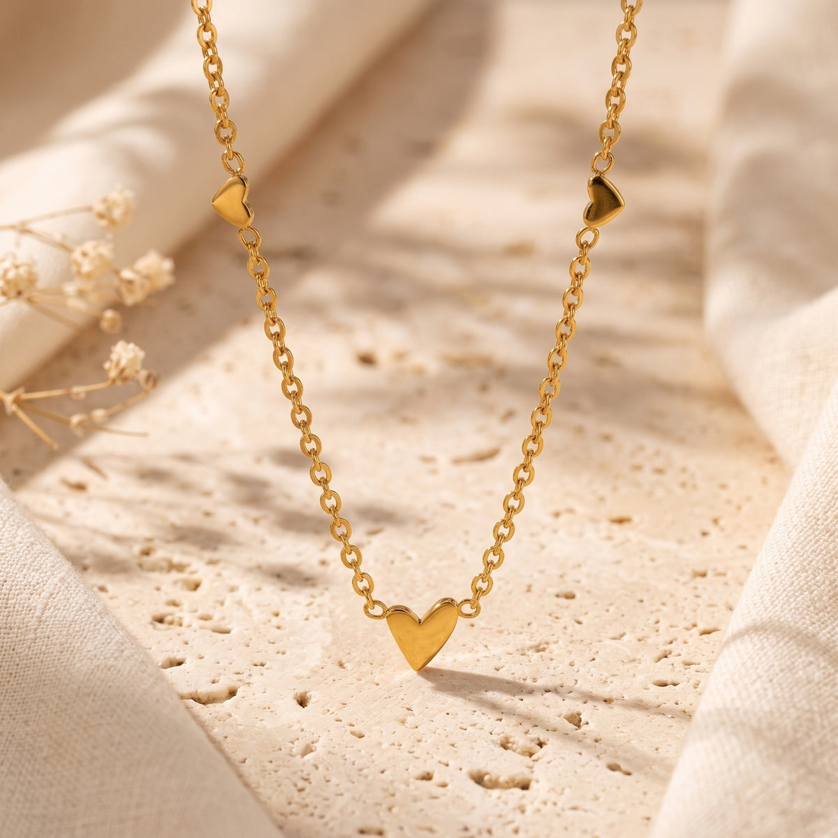 Gold-tone chain necklace with one large and two smaller heart stations draped over a textured stone surface.