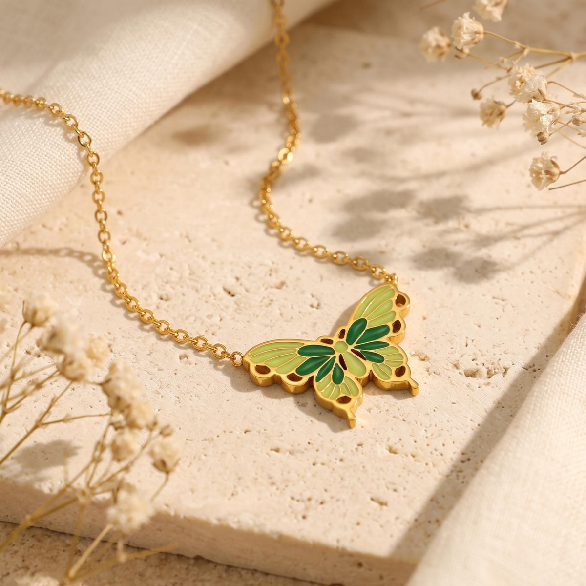 Gold-tone butterfly pendant with green and olive enamel wings on a stone surface.