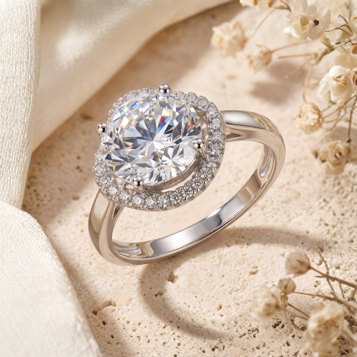 Round halo simulated diamond ring in sterling silver on stone with dried flowers.