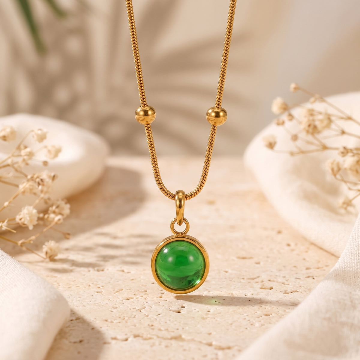 Close-up of a gold-tone snake chain necklace with two station beads and a round green agate cabochon pendant.
