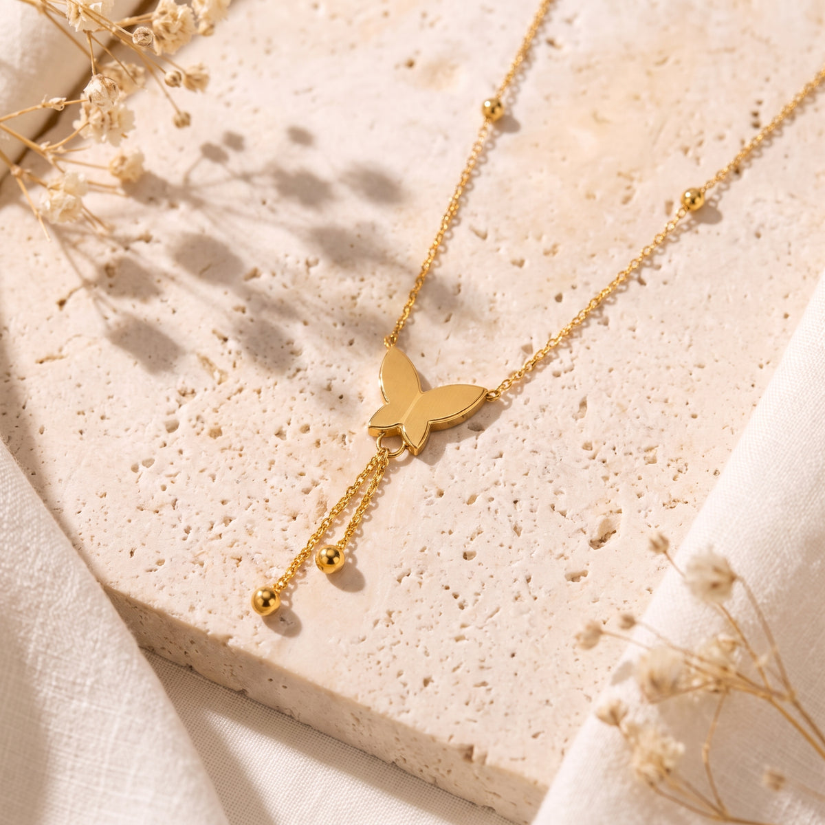 Gold-tone butterfly lariat necklace displayed flat on a textured beige stone slab.