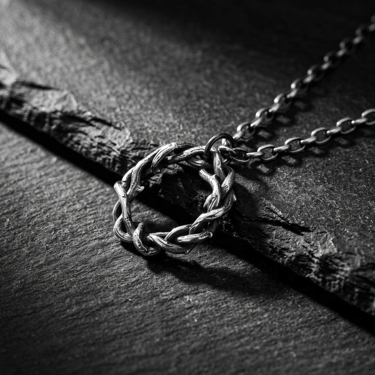 Intertwined silver circular pendant and link chain resting on a dark slate surface.