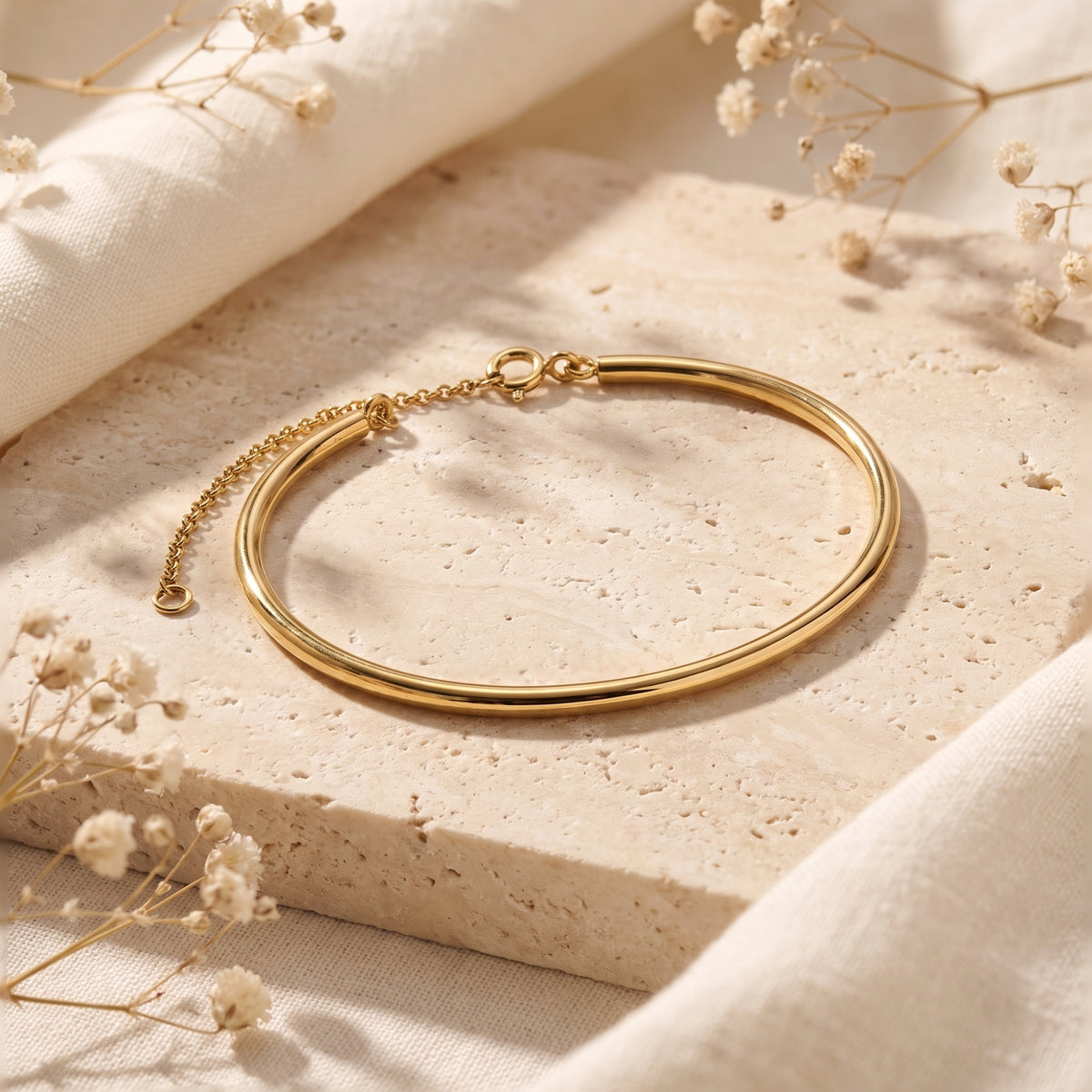 Gold-toned half-bangle bracelet with an extension chain resting on a textured beige stone block.