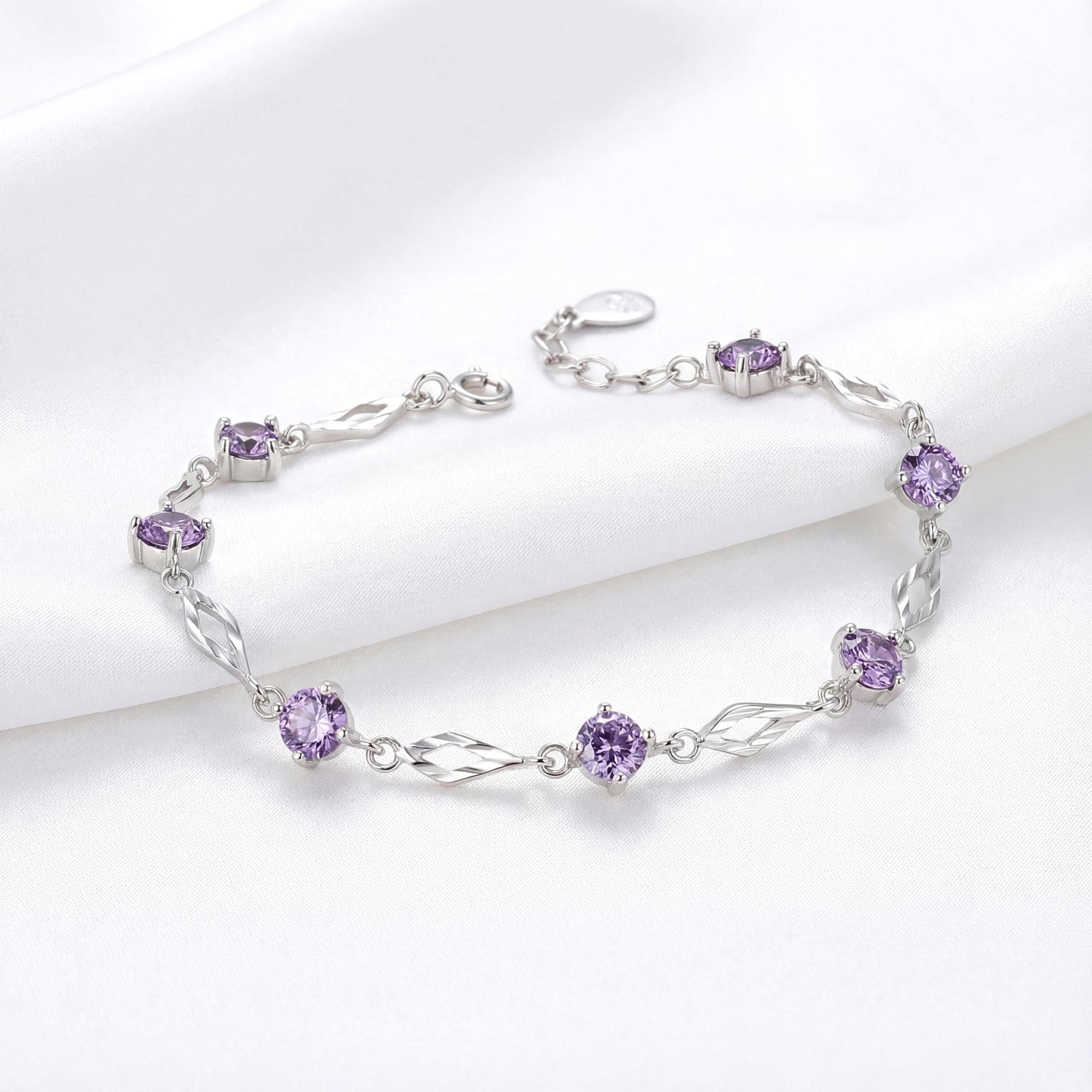 Sterling silver station bracelet with six round-cut simulated amethysts on a white fabric background.