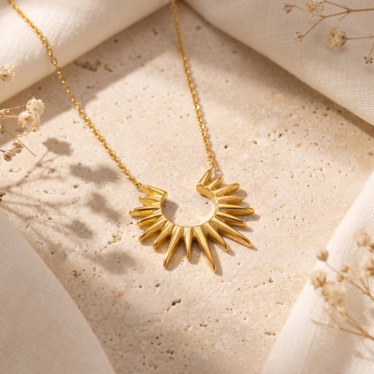 Flat-lay view of the gold-toned sunburst pendant necklace resting on a stone surface with draped fabric.