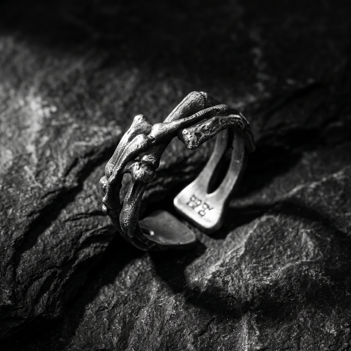 Close-up of the oxidized silver skeletal open band ring with sculpted bone-like forms on textured dark rock.