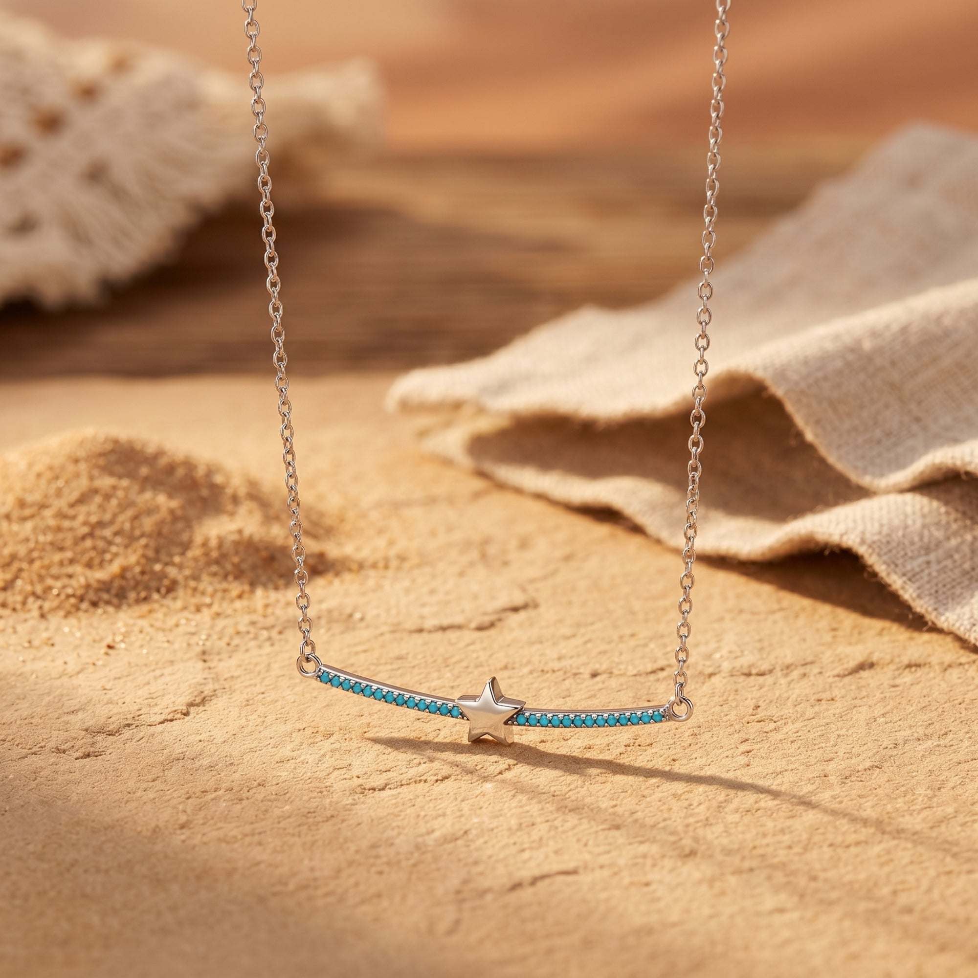 Close-up of the silver Phoenix Star bar necklace with turquoise cabochons on a desert sand and linen background.