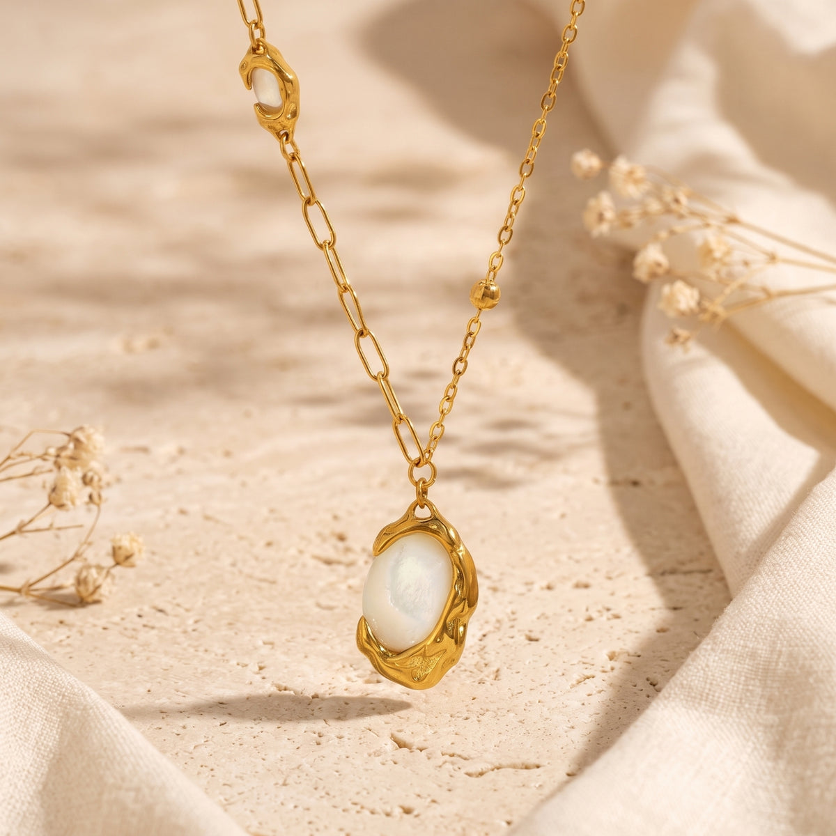 Suspended gold-tone necklace with a molten oval mother-of-pearl pendant and asymmetrical chain.
