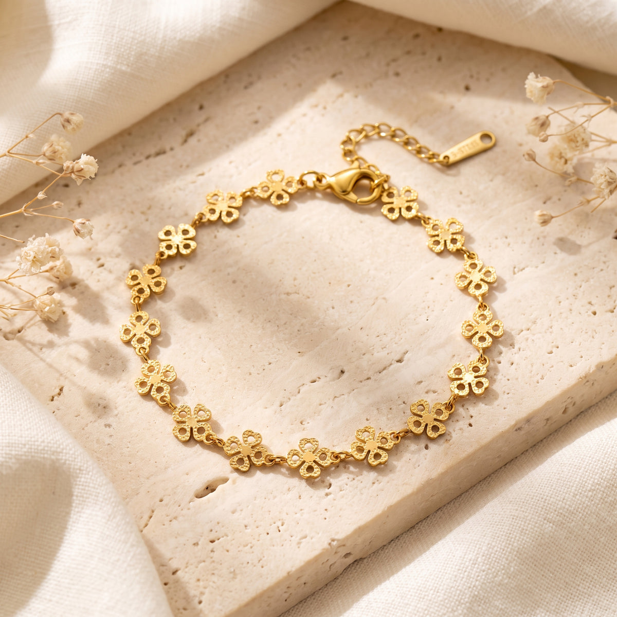 Gold-tone station bracelet with textured four-leaf clover motifs displayed on a beige stone tile.