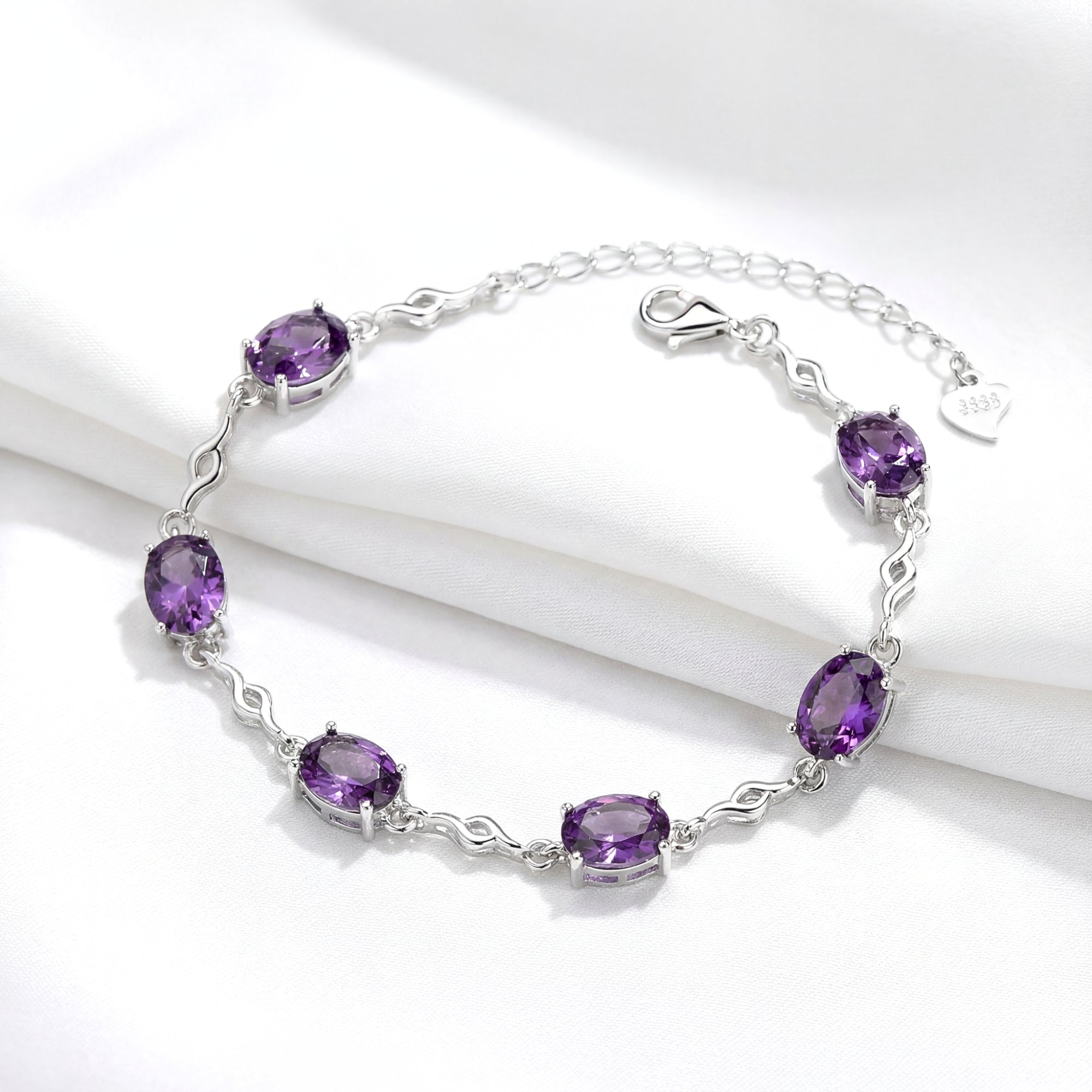 Sterling silver Estella station bracelet with oval-cut simulated amethyst stones and lobster clasp on white fabric.