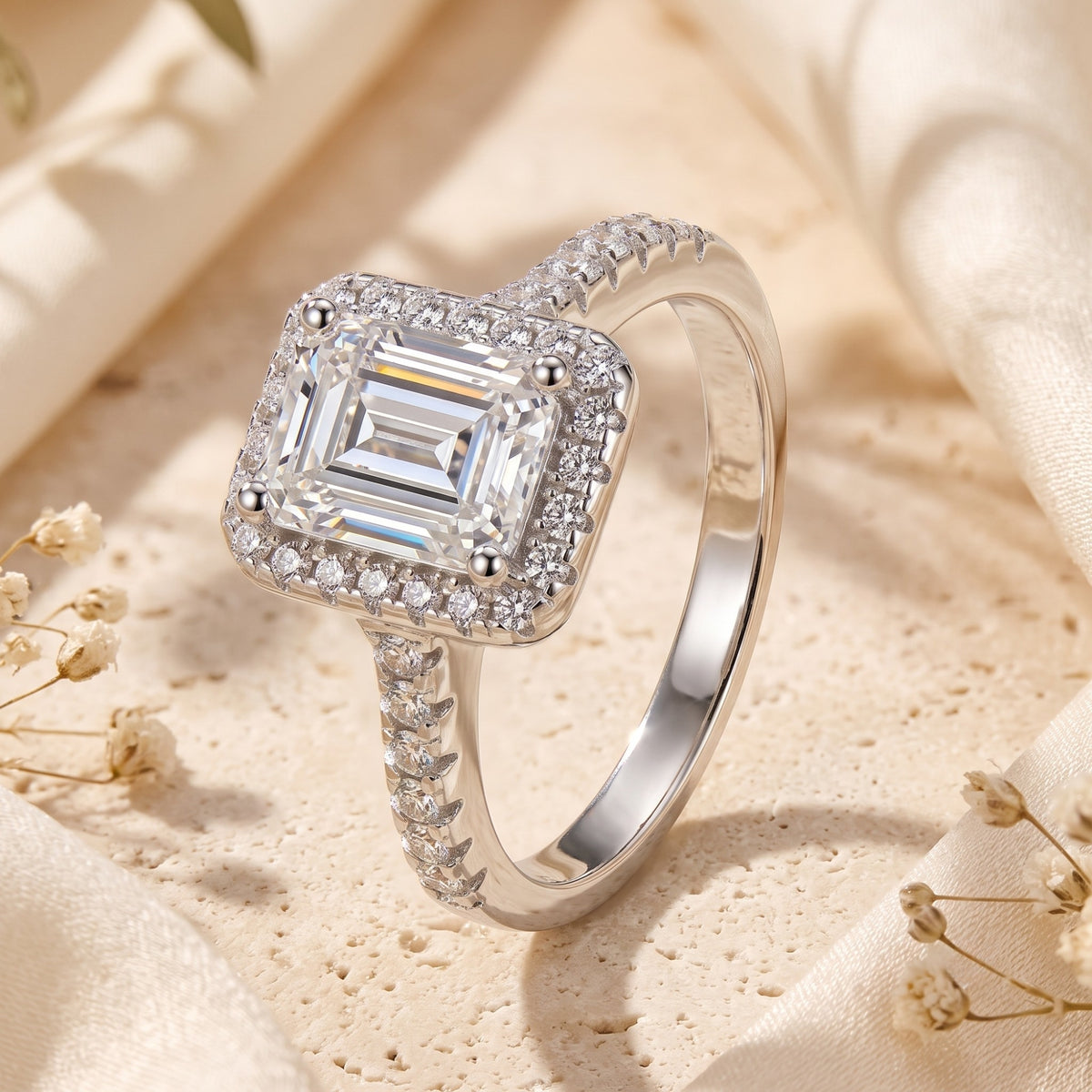 Close-up of a silver-toned ring with an emerald-cut center stone, sparkling halo, and pavé band.