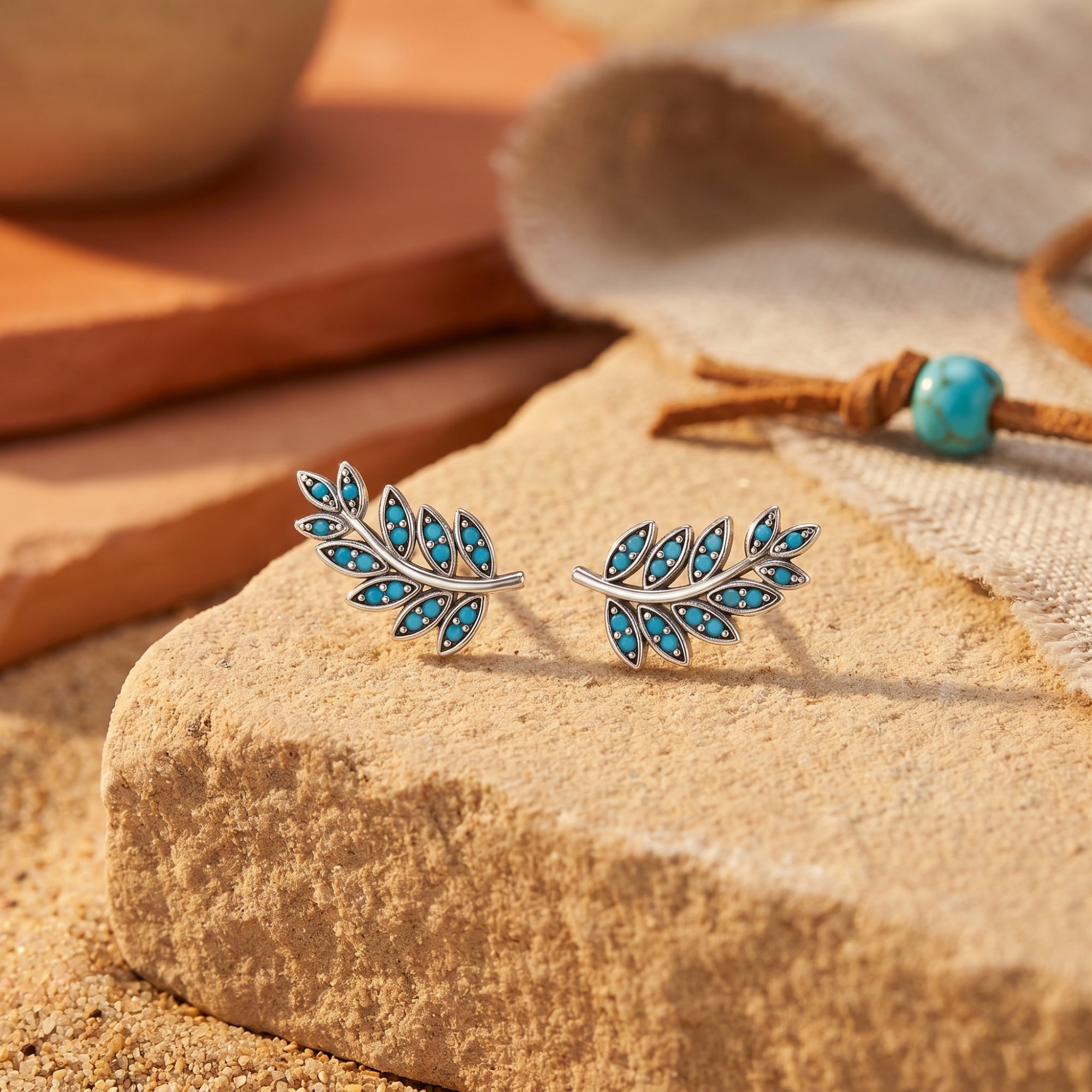 Silver leaf-patterned Taos Turquoise Earrings with round stones on a desert stone with a turquoise bead necklace.