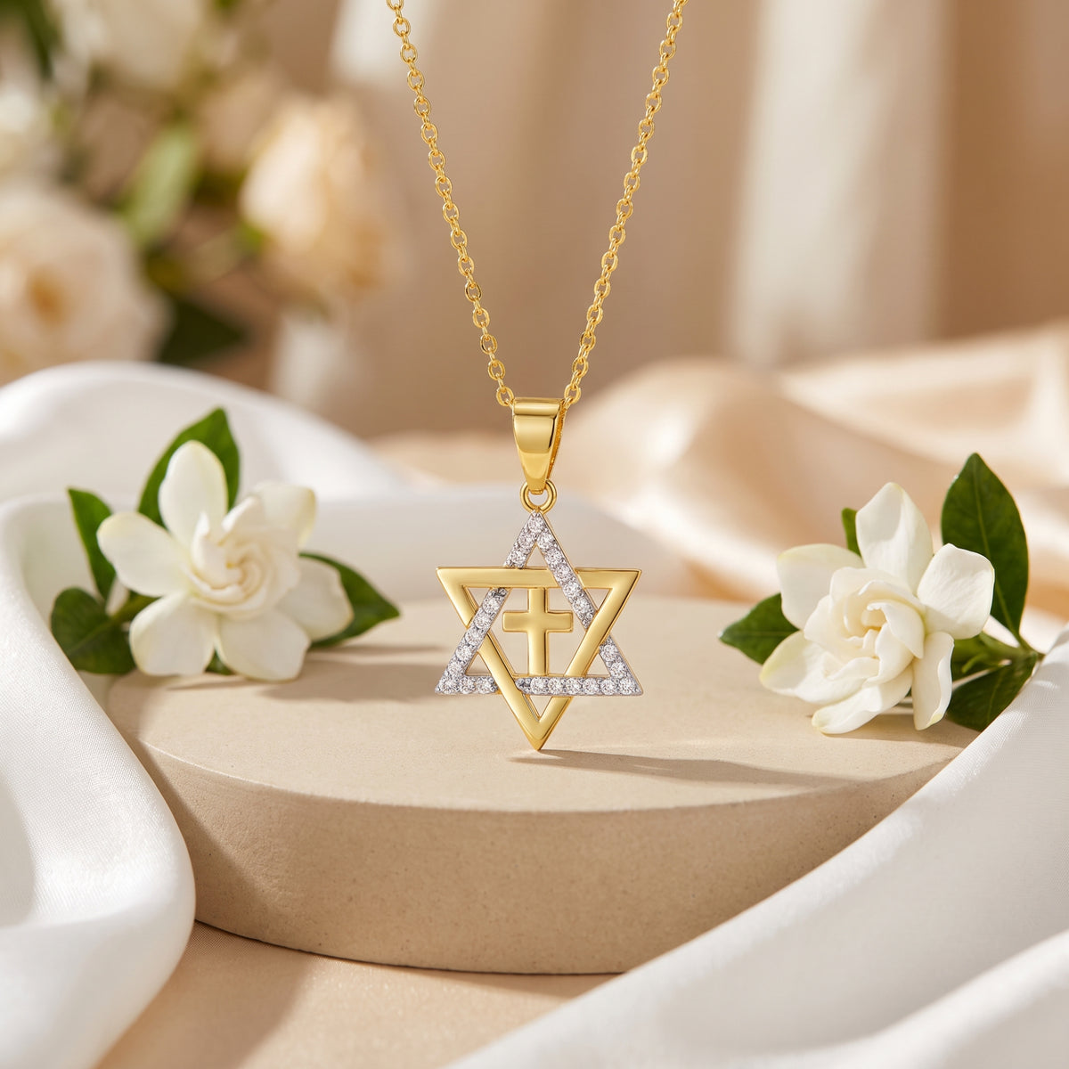Gold-tone Star of David pendant necklace with a center cross displayed on a round pedestal with white flowers.