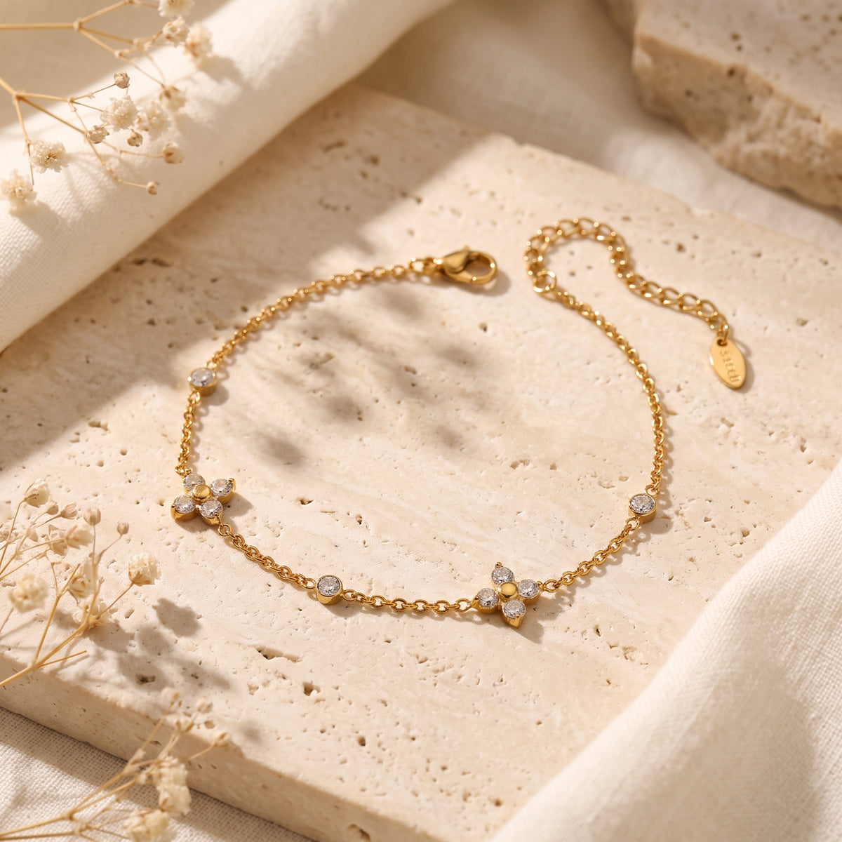 Gold-tone station bracelet with cubic zirconia clovers, displayed on a beige stone slab with dried flowers.