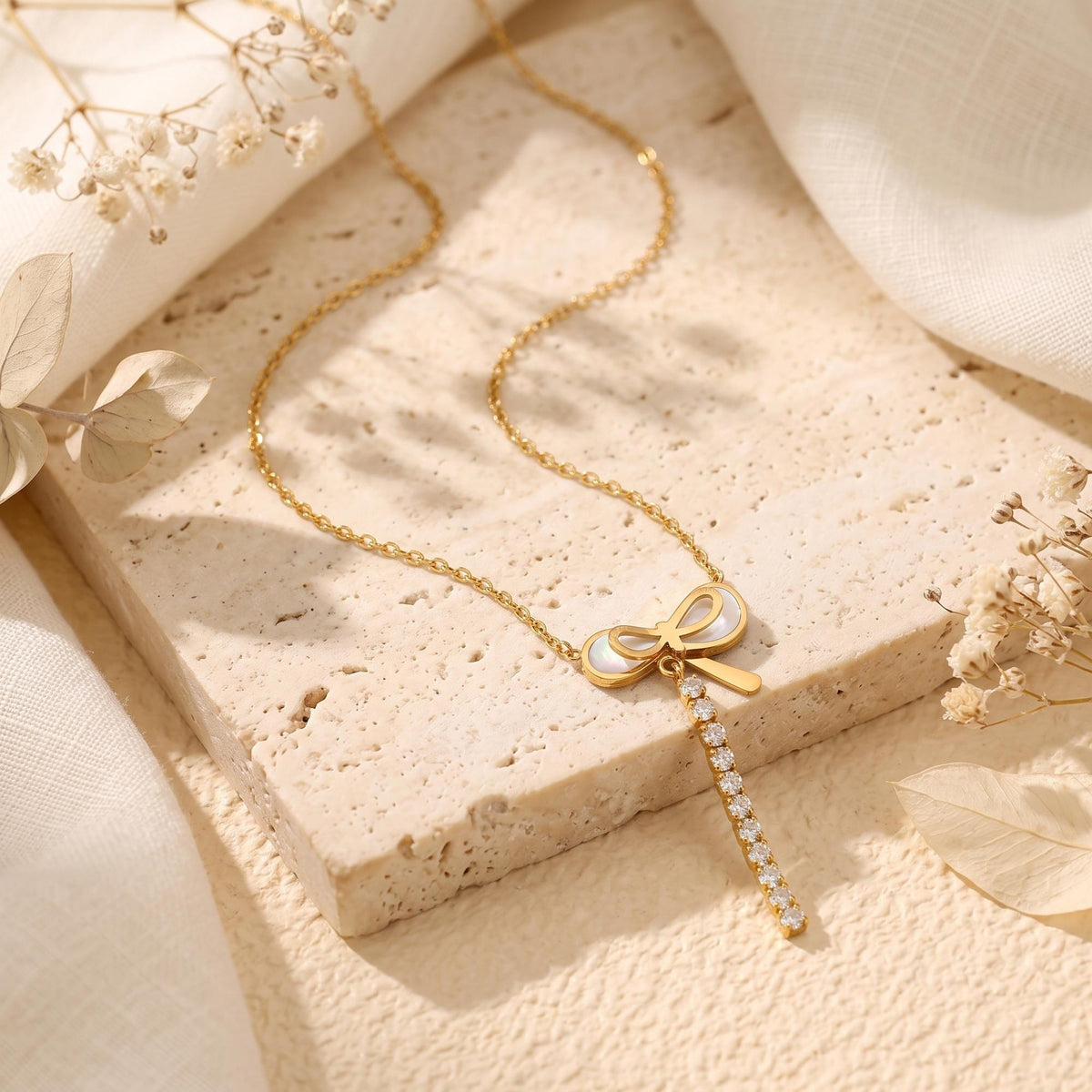 Gold-tone bow necklace with pearlescent inlay and clear stone drop displayed on a textured stone slab.