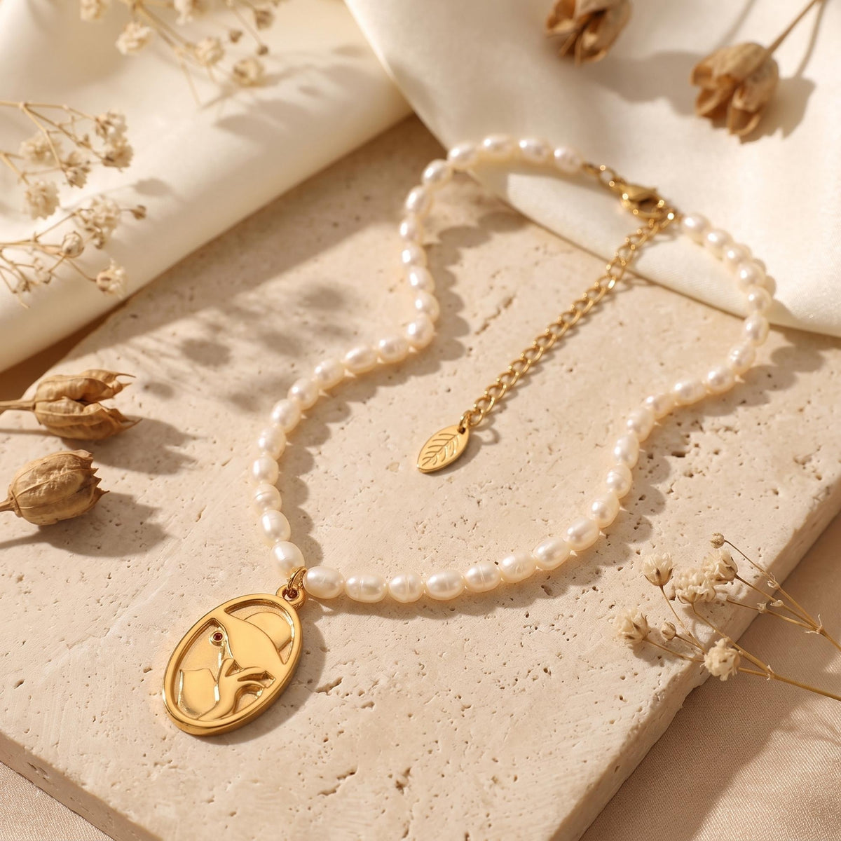 Pearl strand necklace with a gold-tone oval abstract face pendant, displayed with clasp on a stone surface.