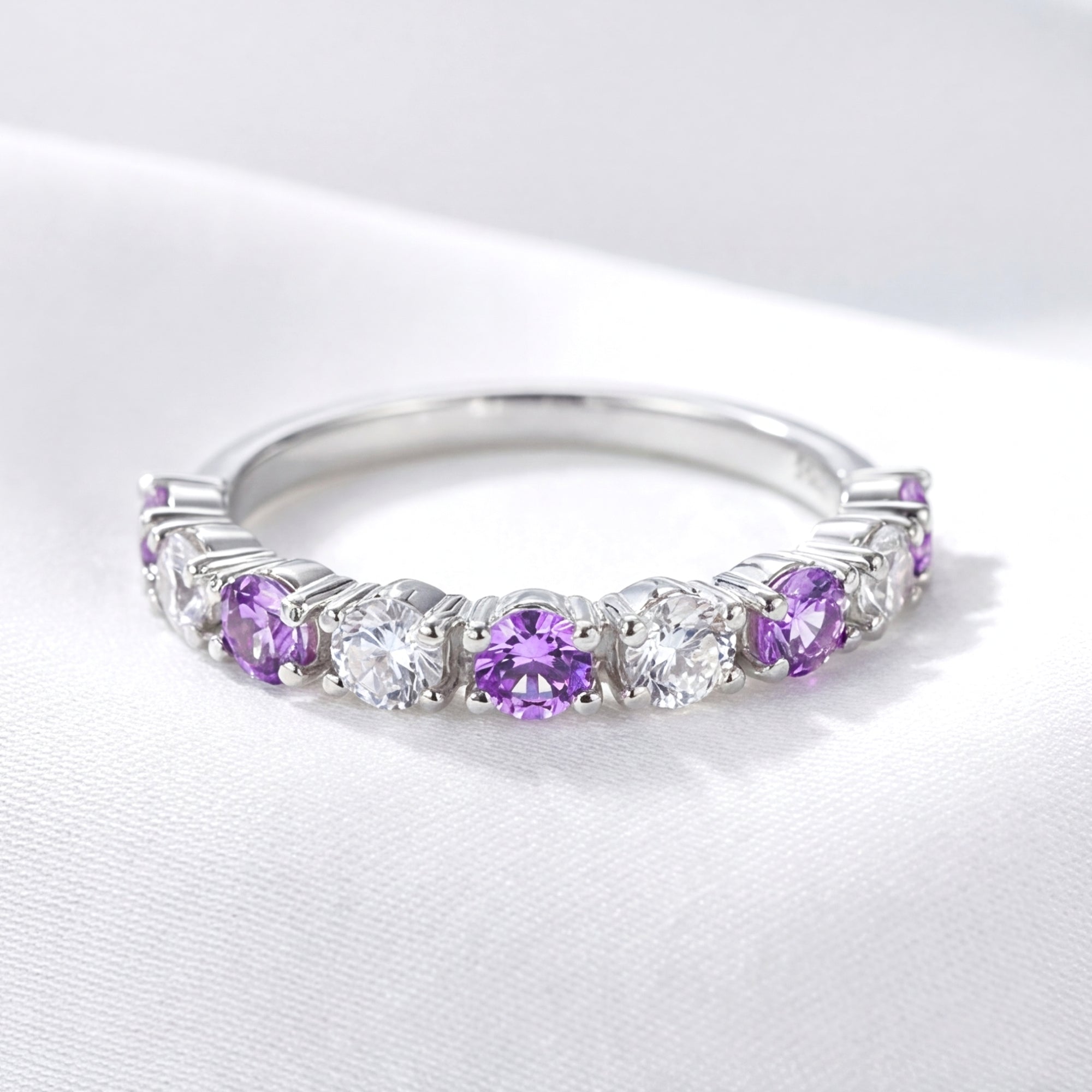 Sterling silver half-eternity ring with round-cut simulated amethysts and clear stones on white fabric.