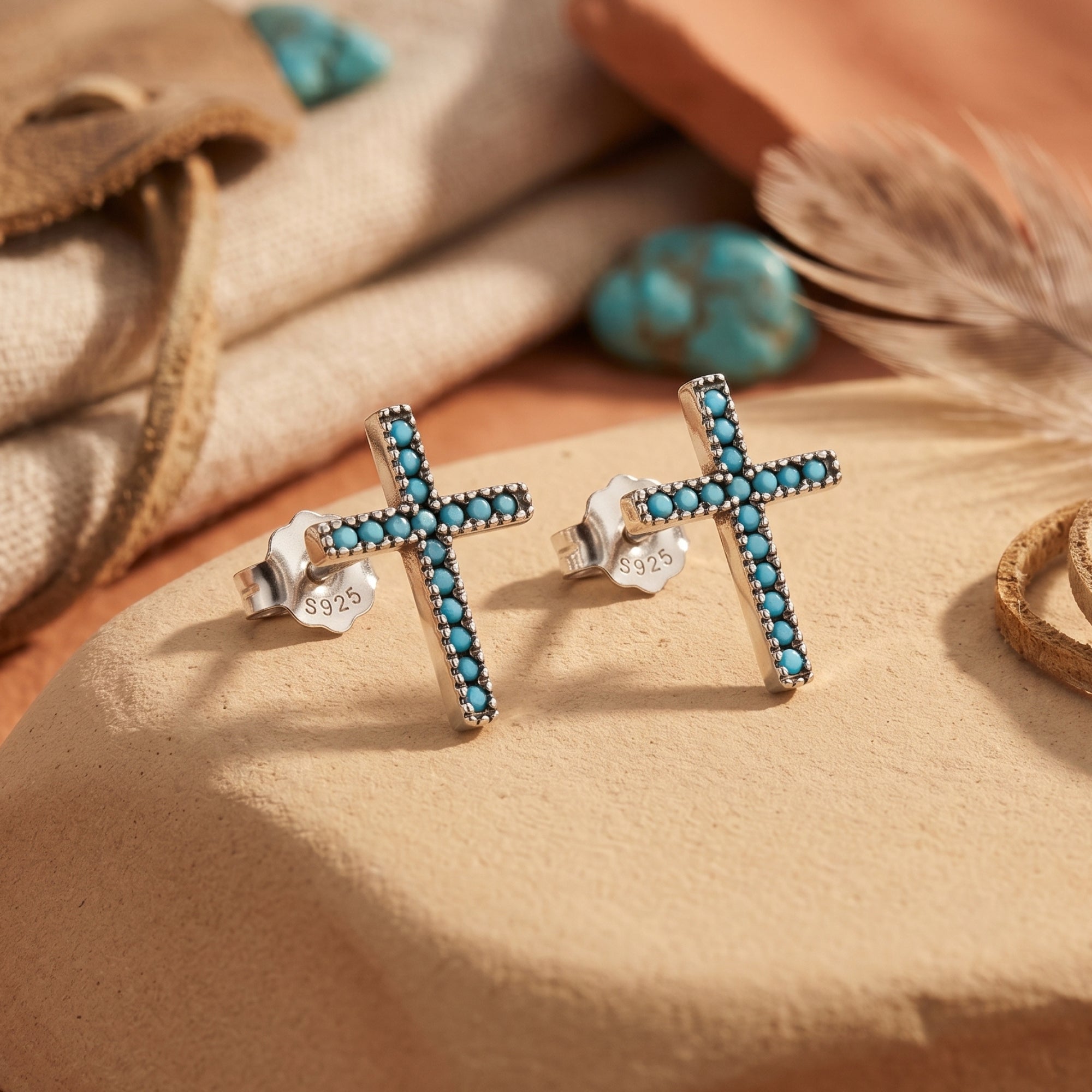 Sterling silver cross stud earrings with round turquoise stones on a desert-inspired stone background.