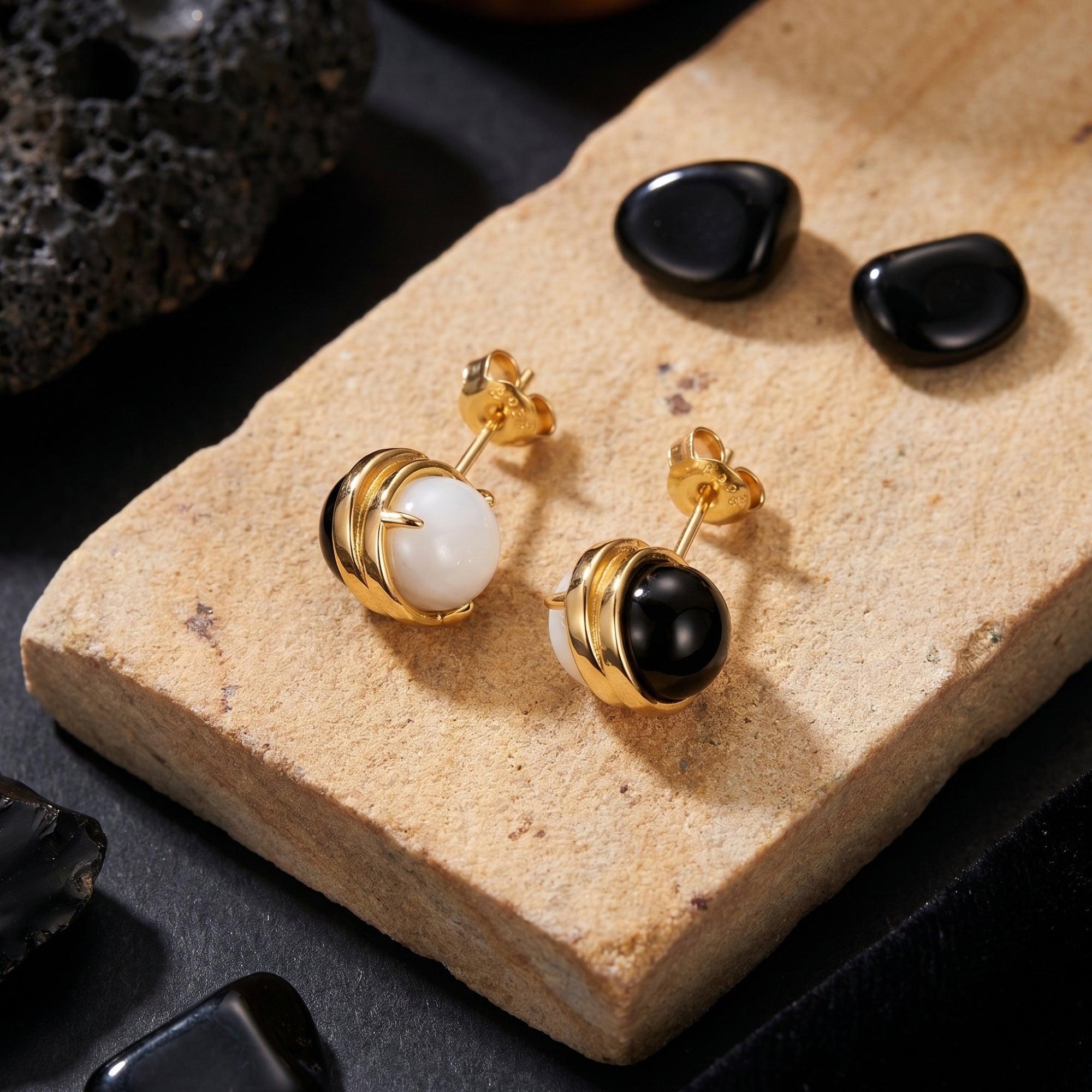18K gold plated Ravenna earrings with round black onyx and white chalcedony stones displayed on a textured stone slab.
