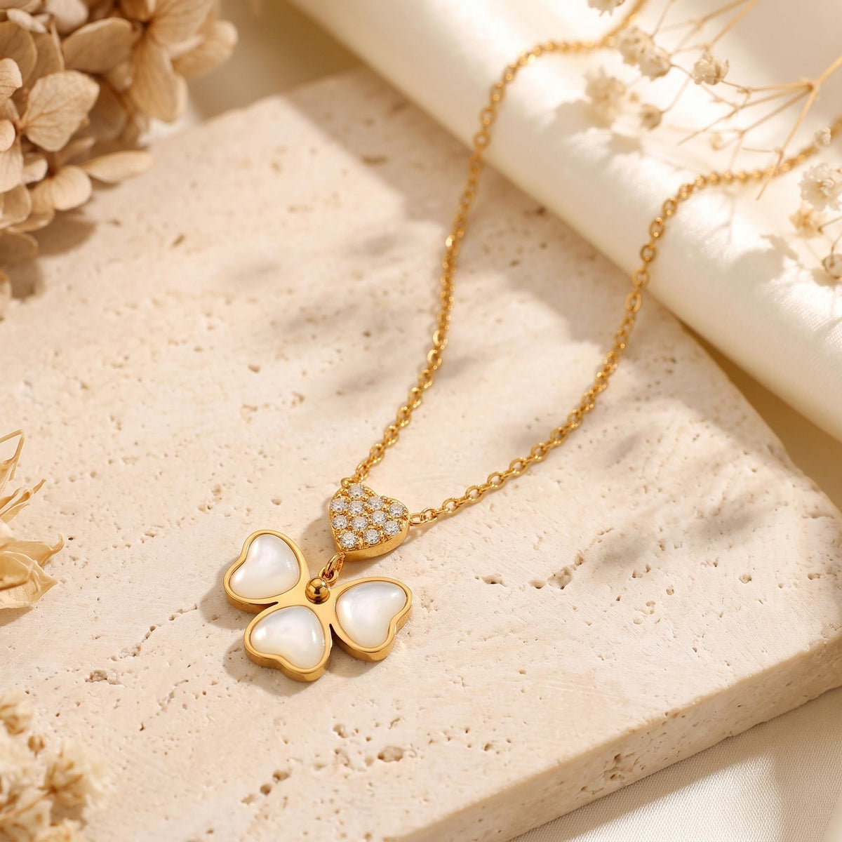 Gold-tone necklace with a mother-of-pearl butterfly pendant and pavé heart, lying on a textured stone surface.