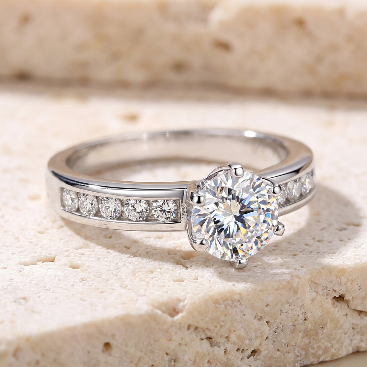 Silver channel-set solitaire ring with a round center stone, resting on a beige stone surface.
