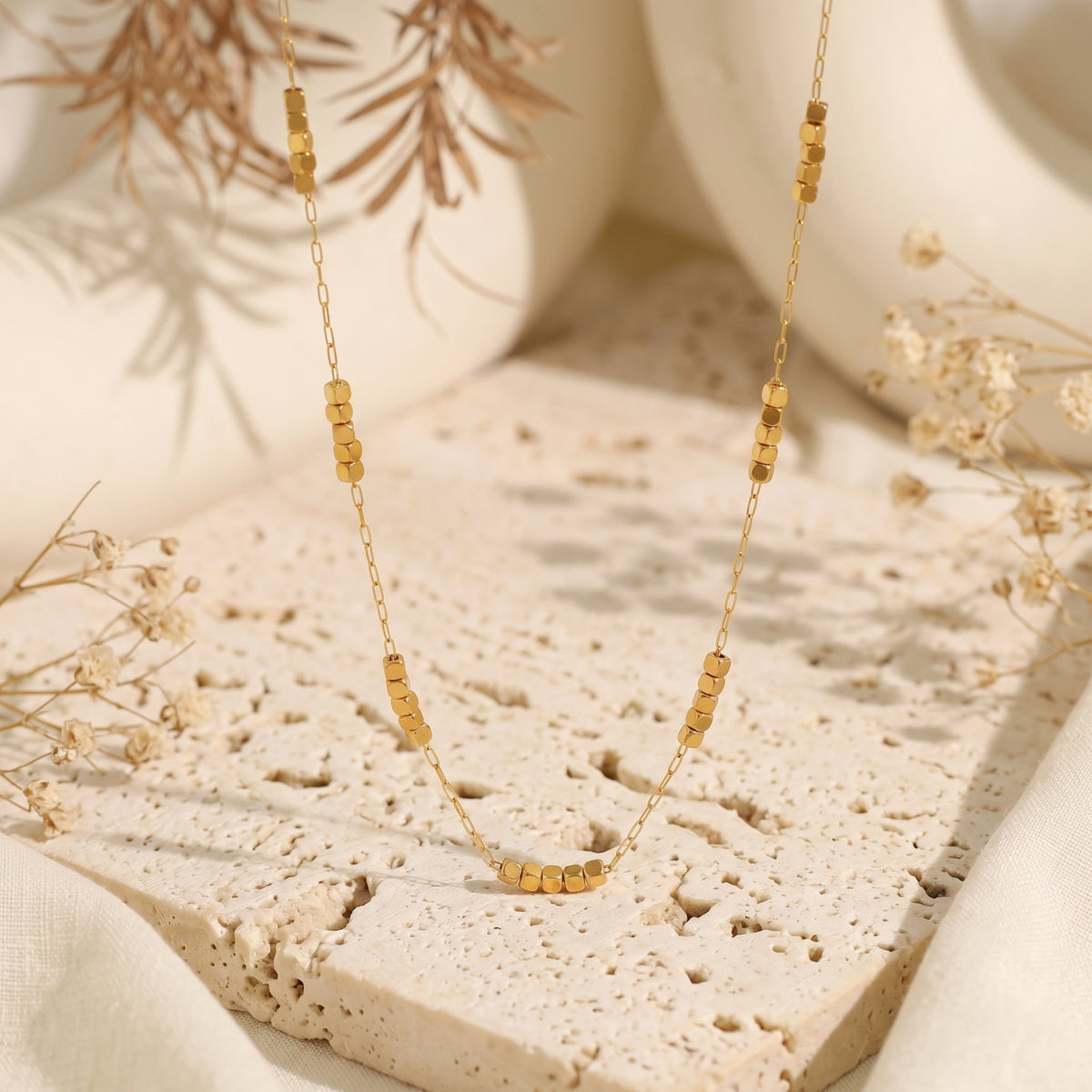 Gold-tone cube station necklace displayed over a textured stone block.