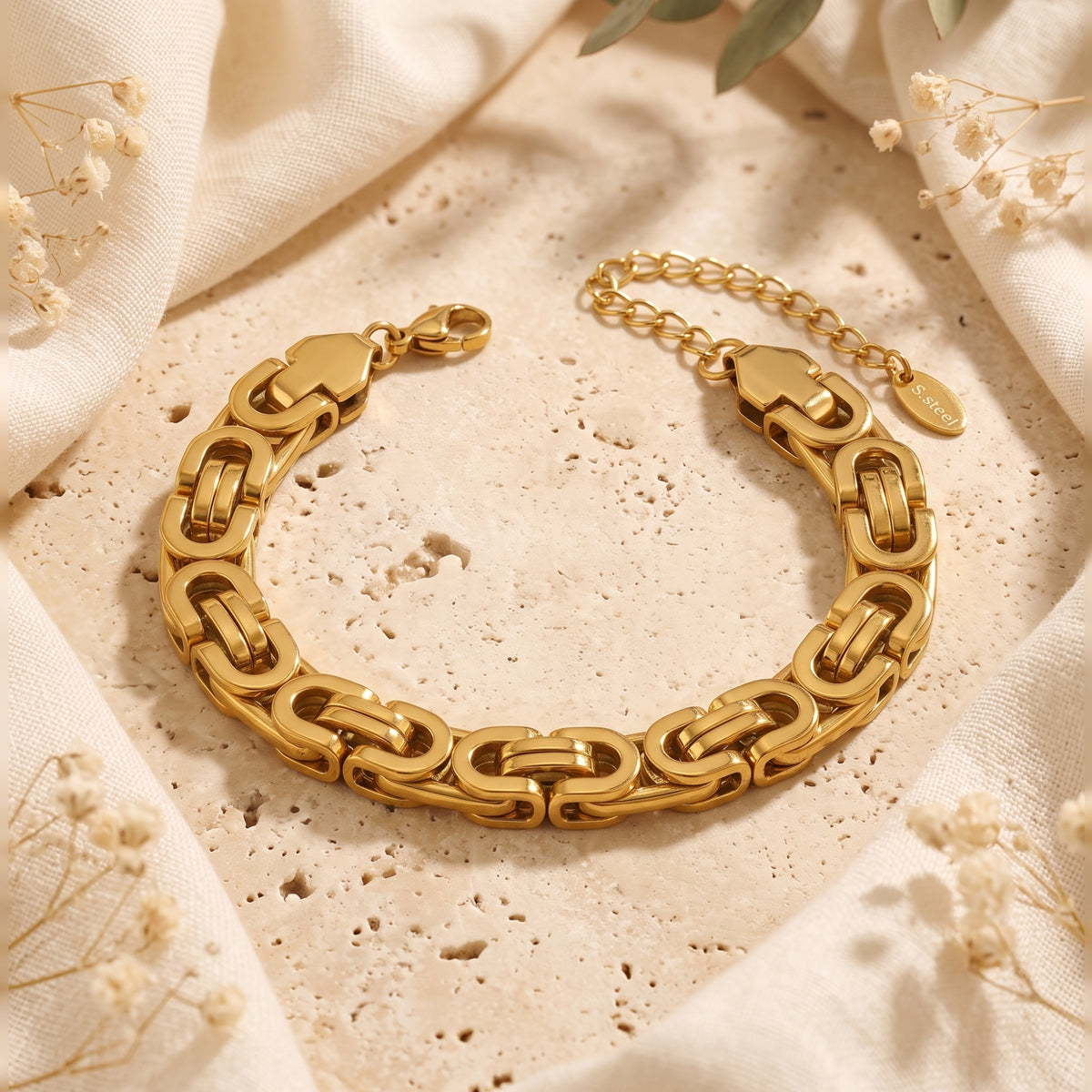 Gold-toned Byzantine link bracelet with extension chain, laid flat on a beige stone surface.