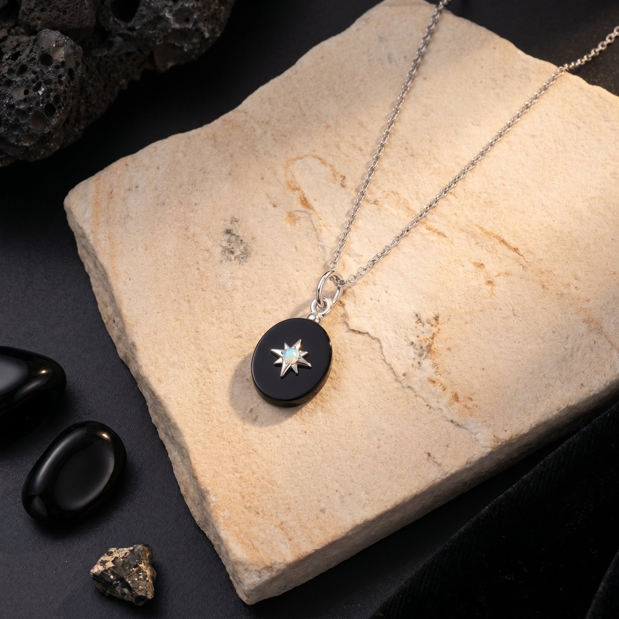 Oval black onyx pendant necklace in silver with a starburst center, displayed on a natural stone slab.
