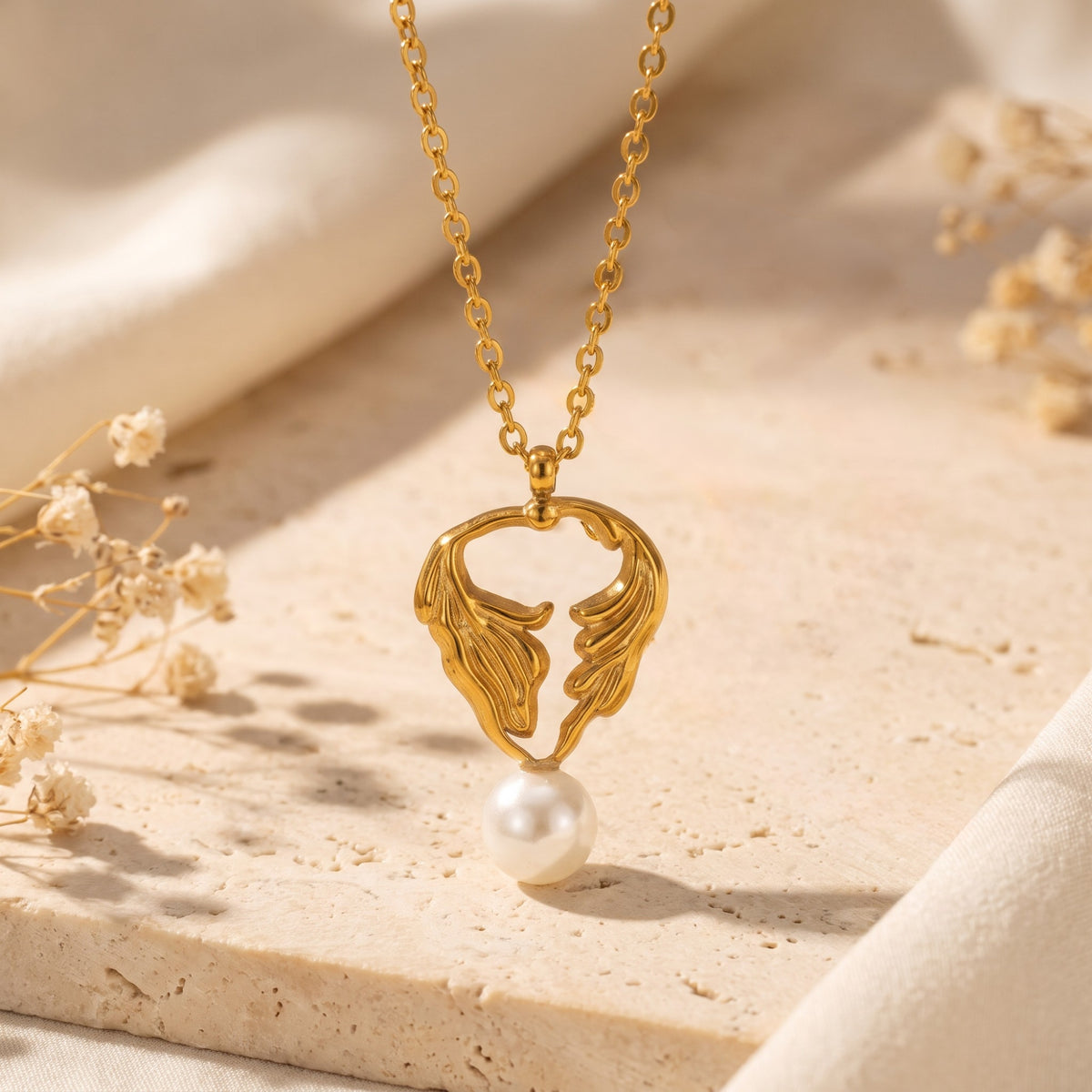 Close-up of the gold-tone leaf pendant with a white pearl drop over a stone surface.