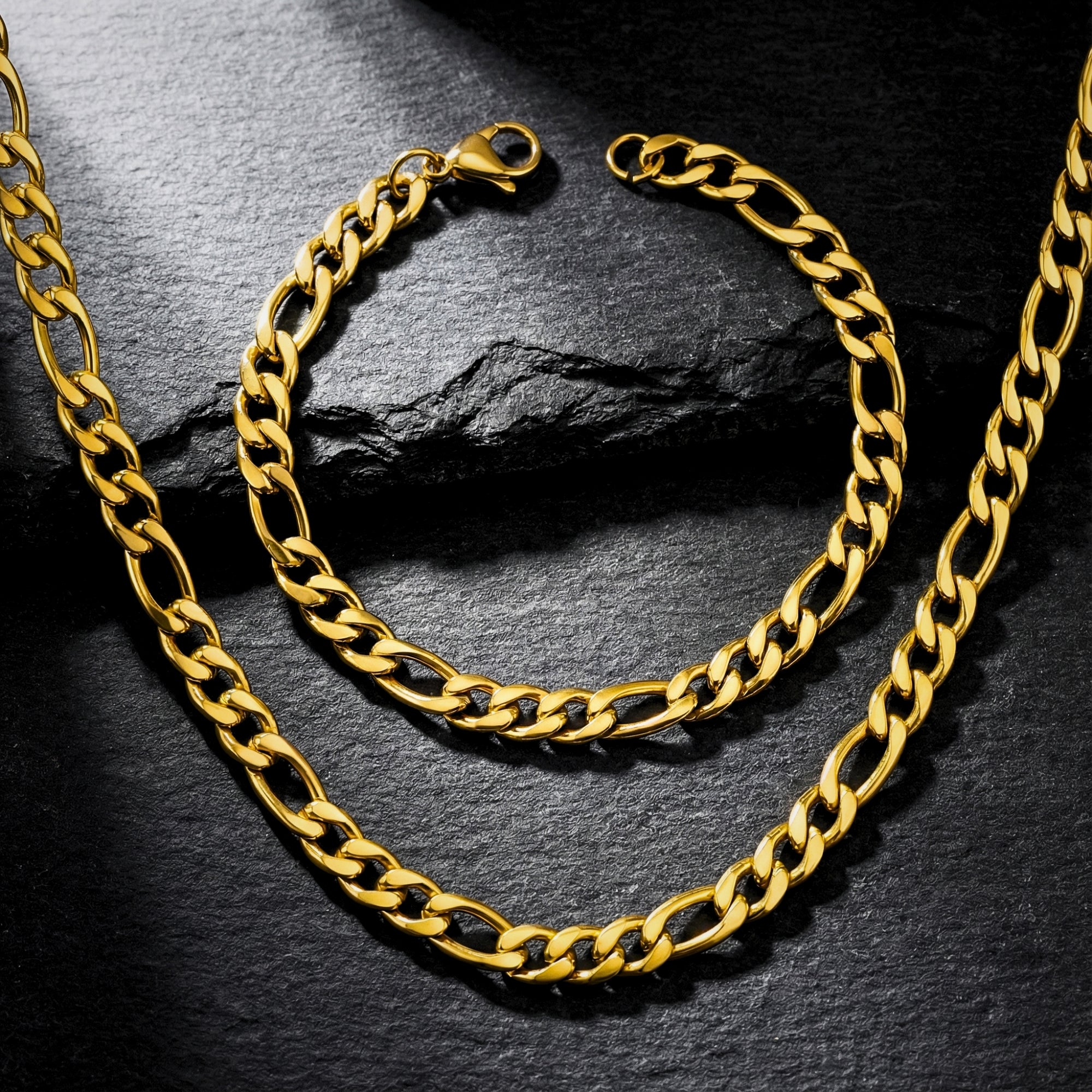 Gold Figaro chain and bracelet set on a dark stone background, showing the 8mm link detail and lobster clasp.