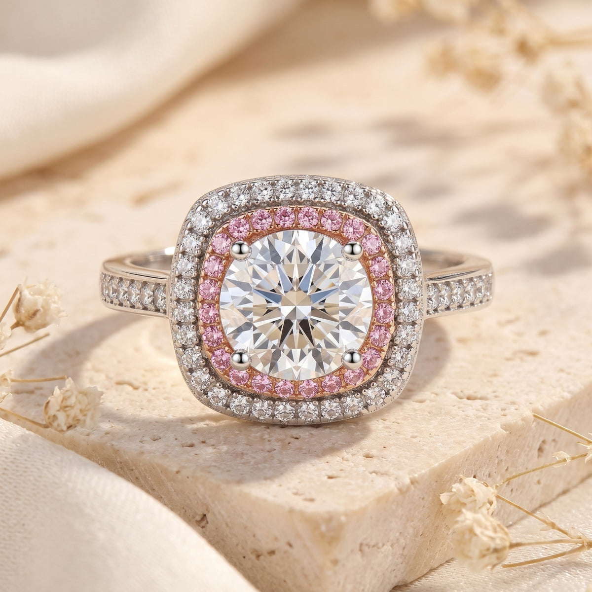 Close front view of a cushion-shaped dual-halo ring with a round clear center stone, pink inner halo, and white outer halo.