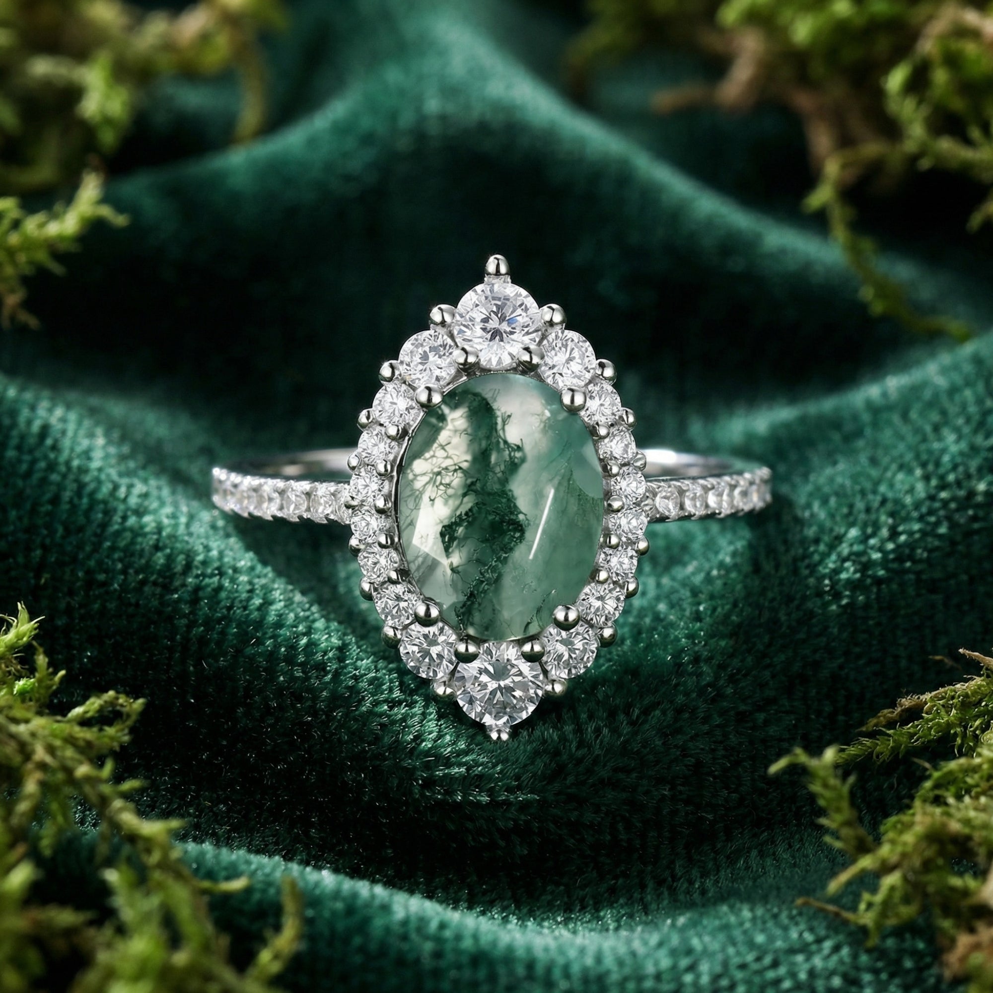 Top view of an oval moss agate halo ring in S925 sterling silver on green velvet with decorative moss.
