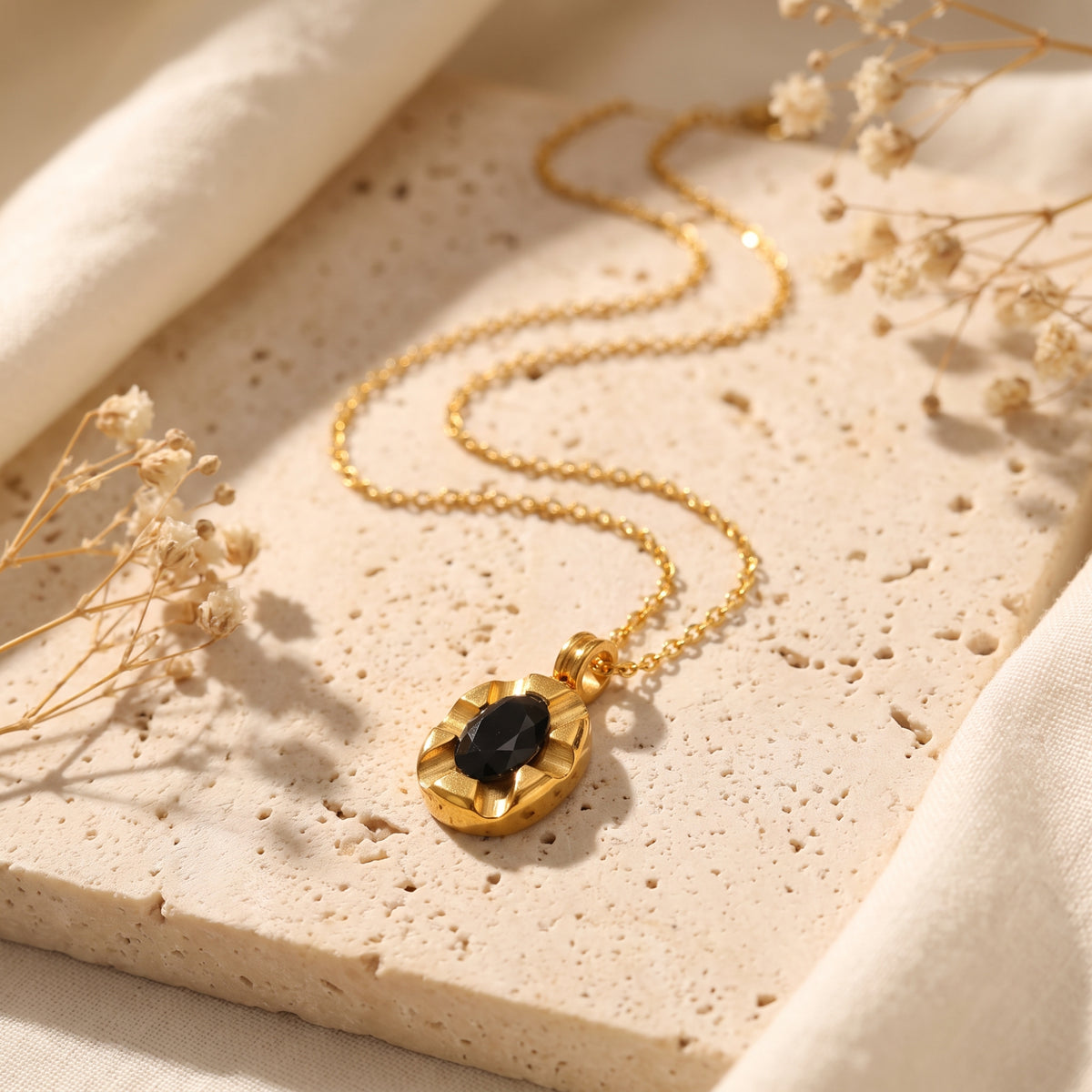 Gold-finish necklace with a fluted oval medallion pendant and black cubic zirconia, laid flat on a textured stone slab.