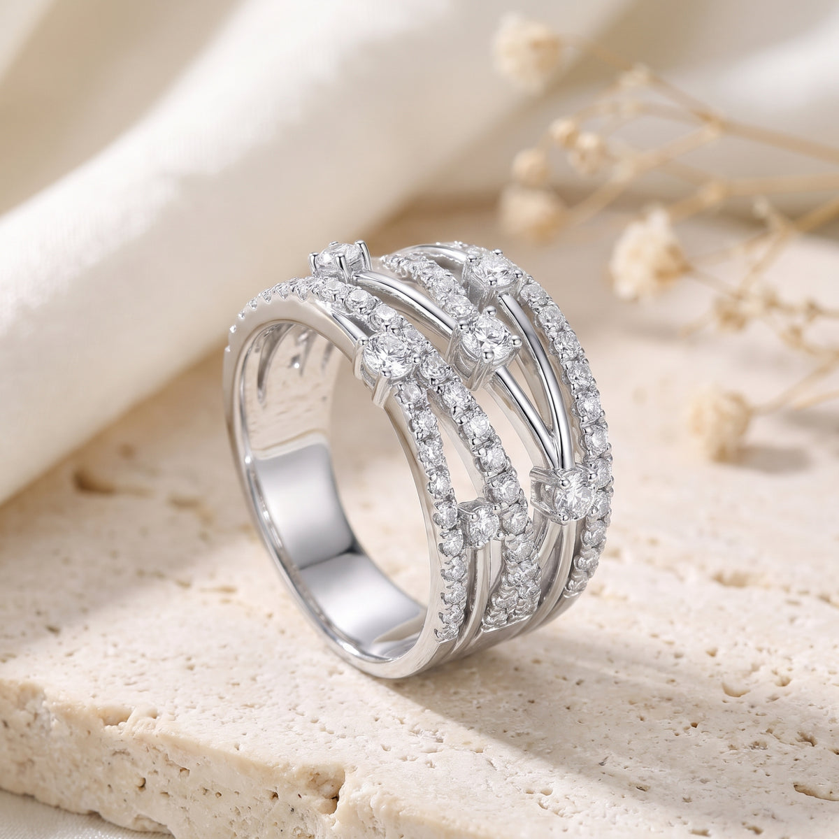 Close-up of a silver multi-row criss-cross ring with clear stones on a neutral stone surface.