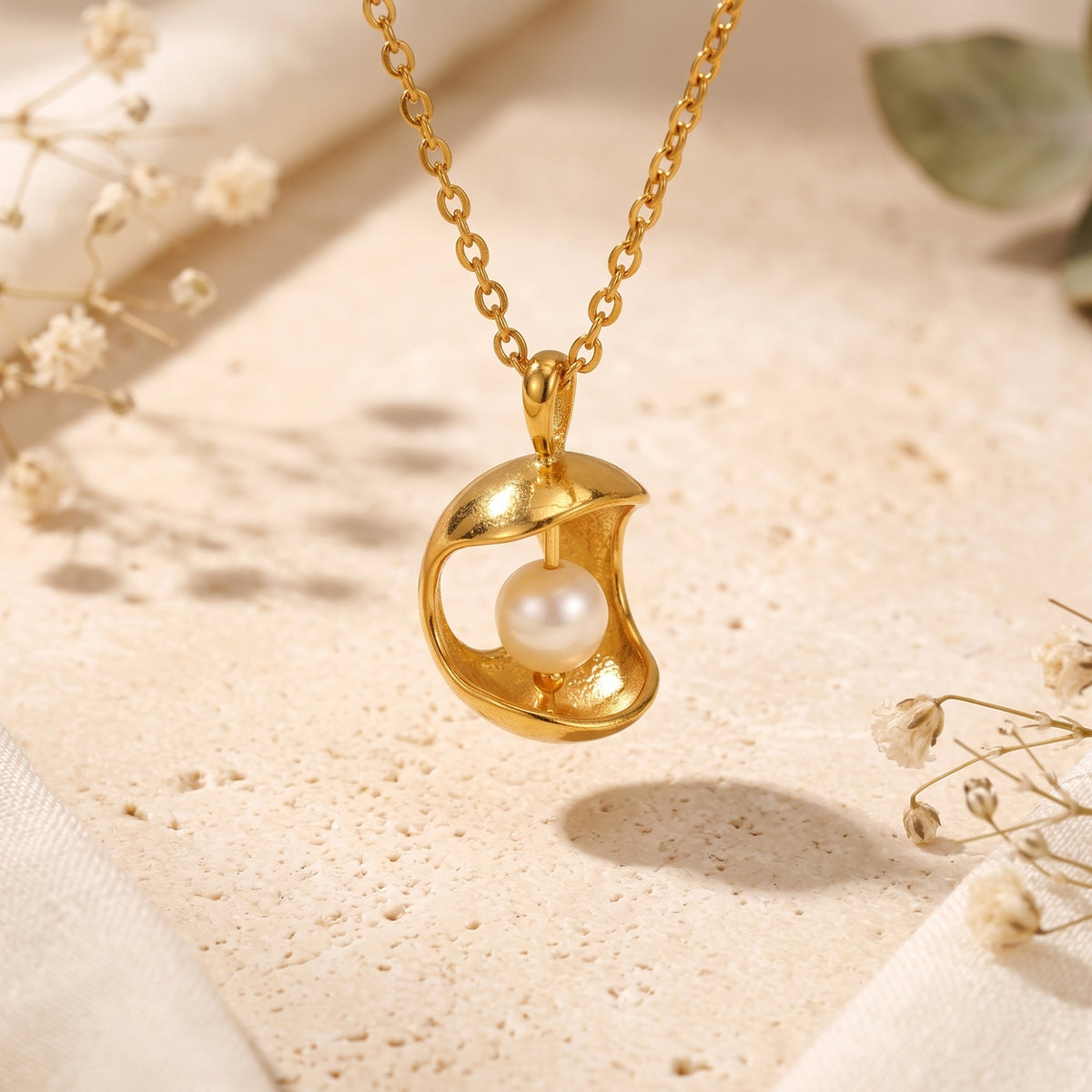 Close-up of a gold-tone crescent pendant holding a luminous white pearl on a fine chain.