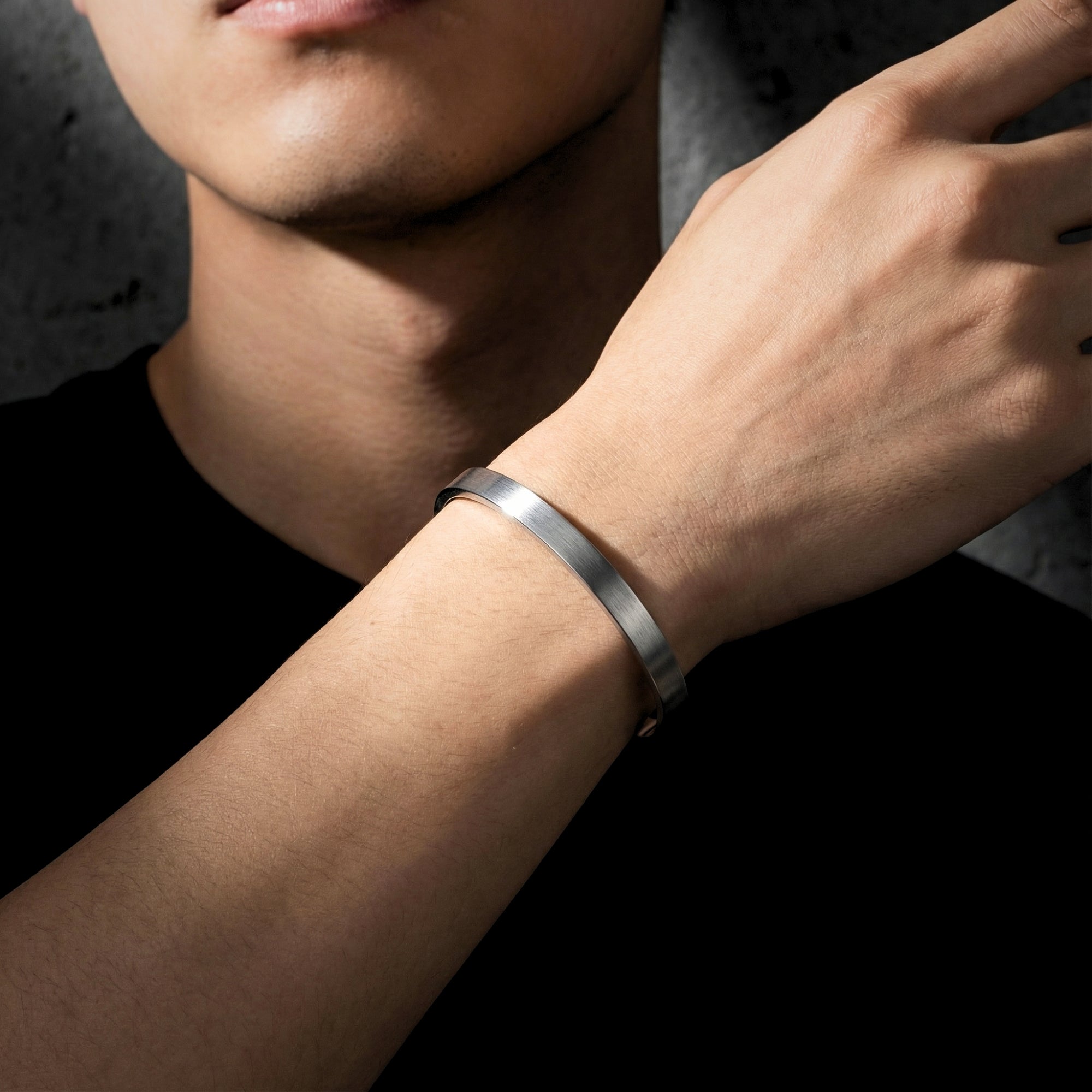 Close-up of a silver stainless steel cuff bracelet with a brushed finish on a man's wrist.