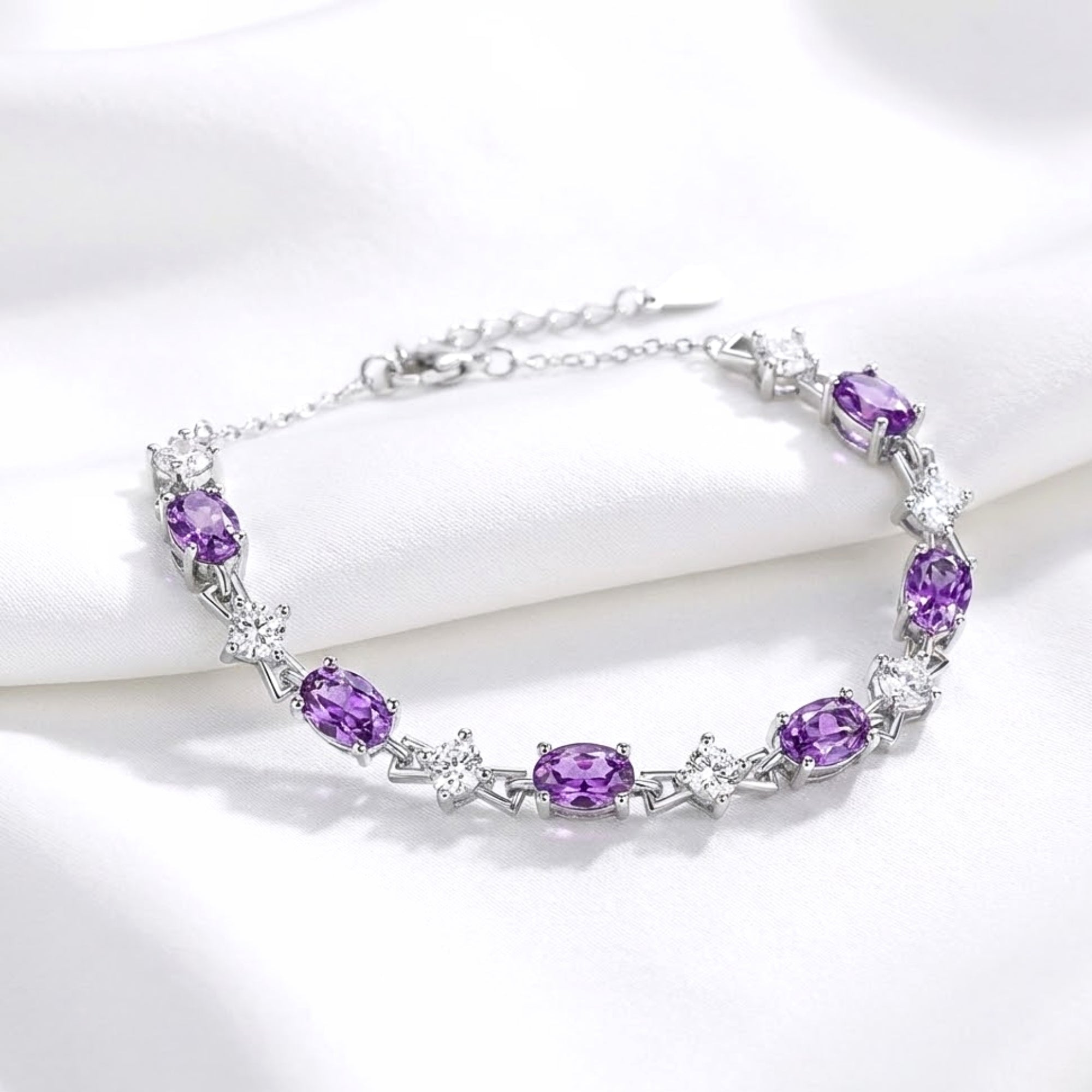 Side view of the Lucina silver tennis bracelet with oval cut purple amethysts and round accents on white silk.