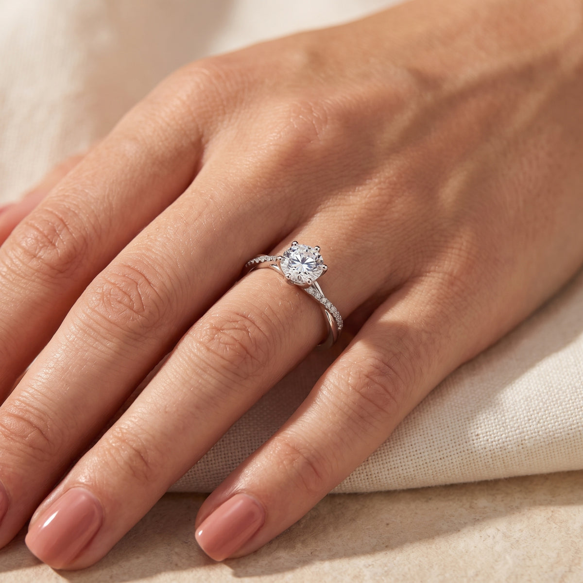 Silver crossover ring with a round clear center stone worn on a hand over cream-colored fabric.