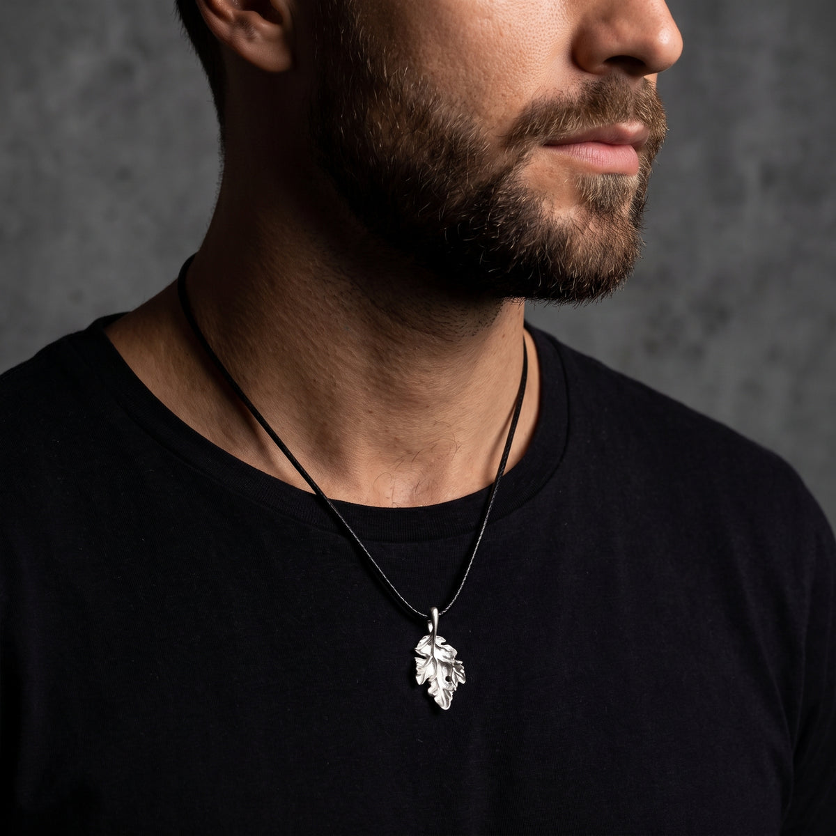 Bearded man wearing a silver oak leaf pendant on a black cord over a black T-shirt.