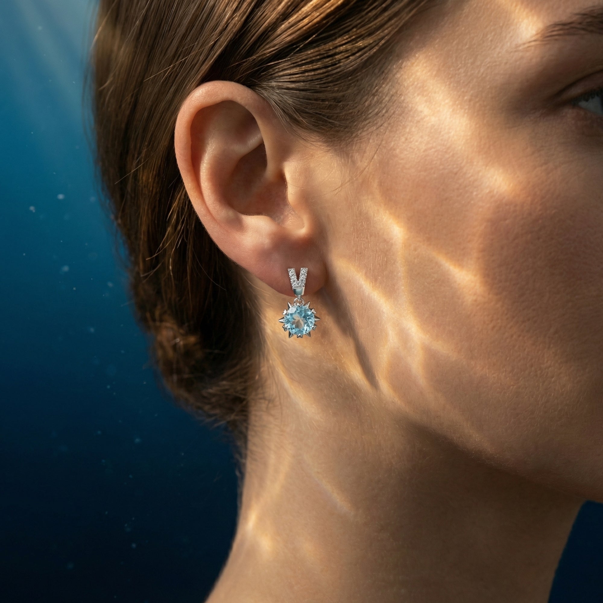 Woman wearing a round cut aquamarine drop earring in platinum with a diamond-accented V-shaped post.