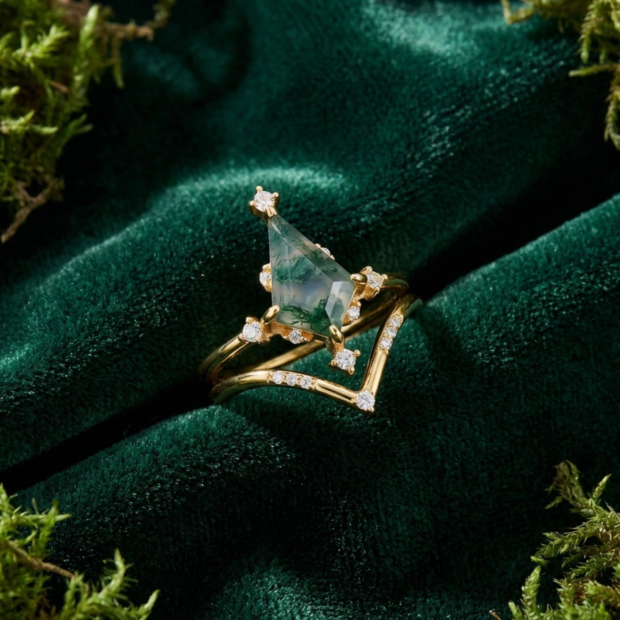 Macro view of a kite cut moss agate gold ring set resting on dark green velvet fabric.
