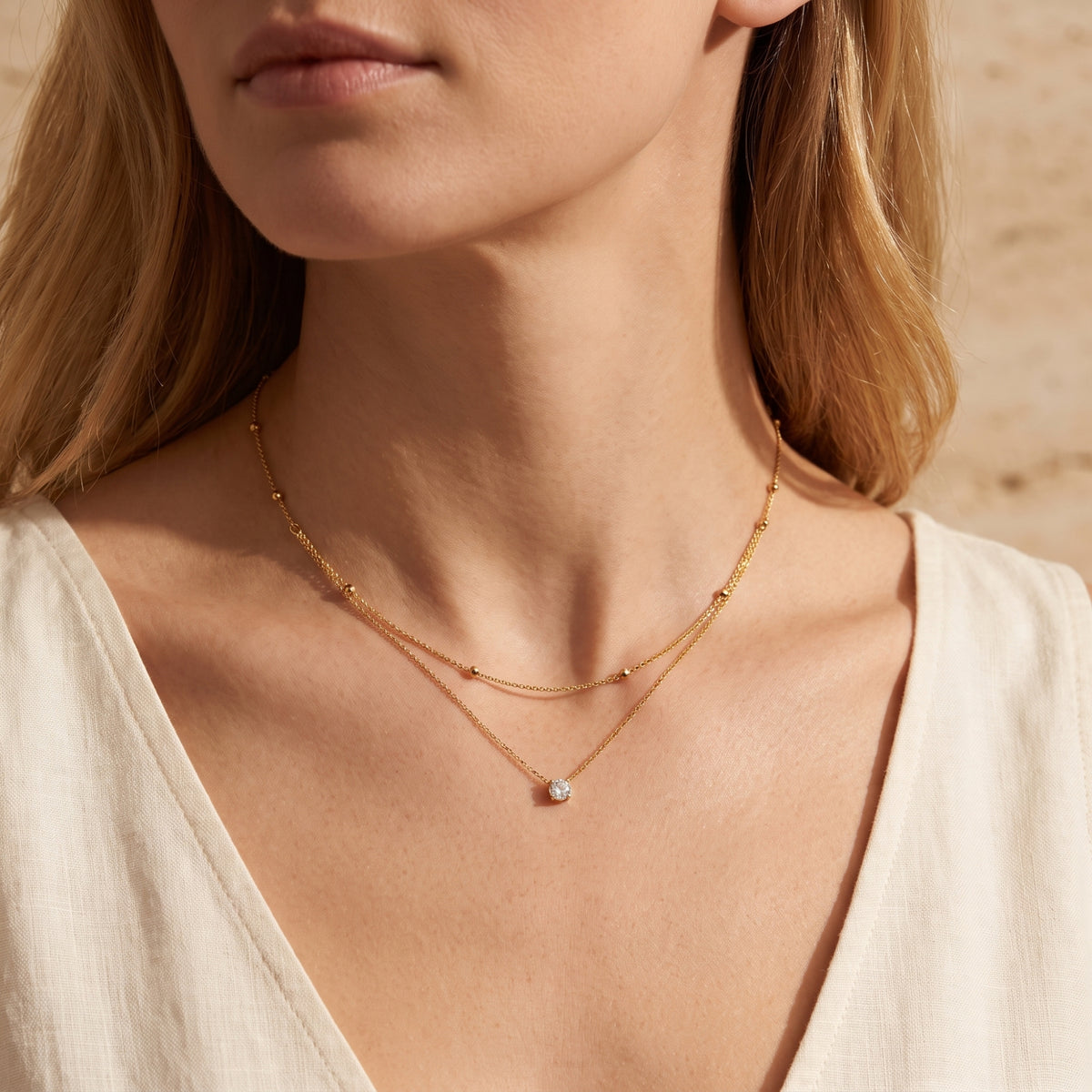 Front view of a model wearing the gold-tone layered necklace with beaded upper strand and centered solitaire pendant.