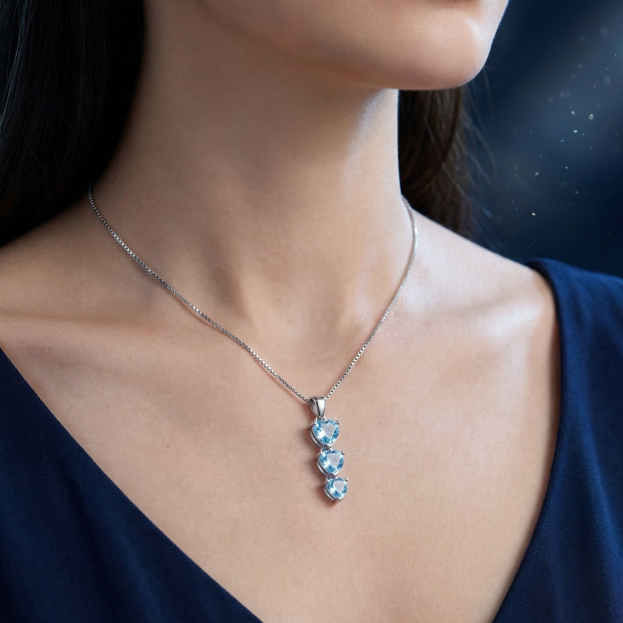 Woman wearing the silver Amora Trio necklace with three heart cut blue topaz gemstones.