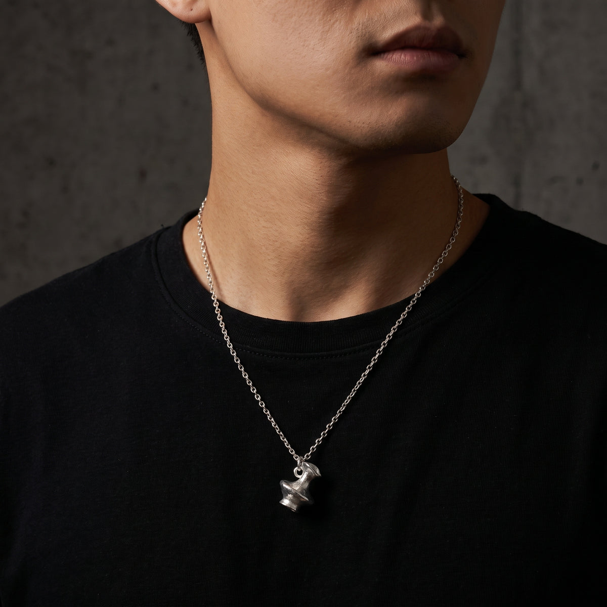 Silver vessel pendant necklace worn over a black T-shirt, shown in a close chest-up view.
