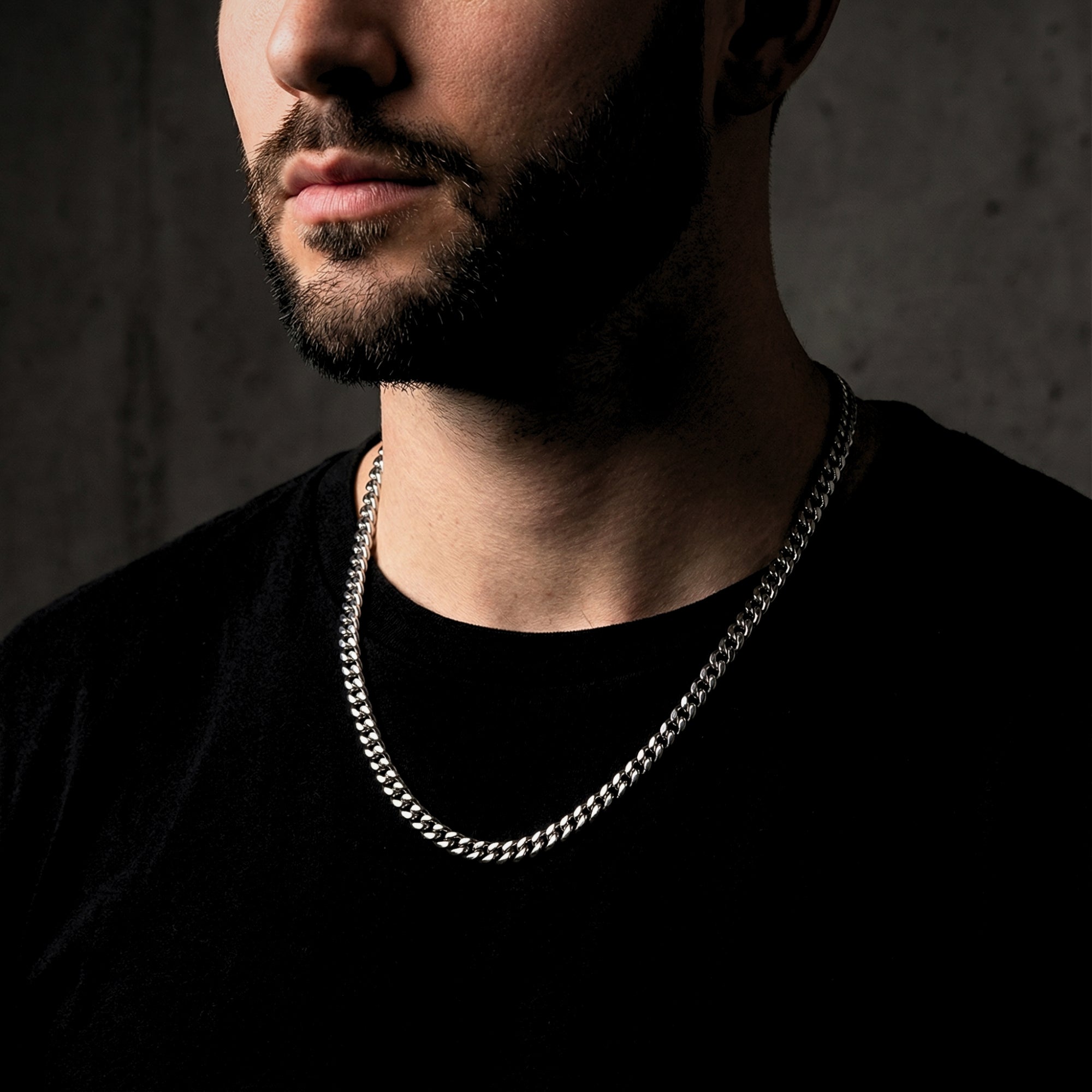 Men's silver stainless steel Cuban link chain worn by a model over a black t-shirt.